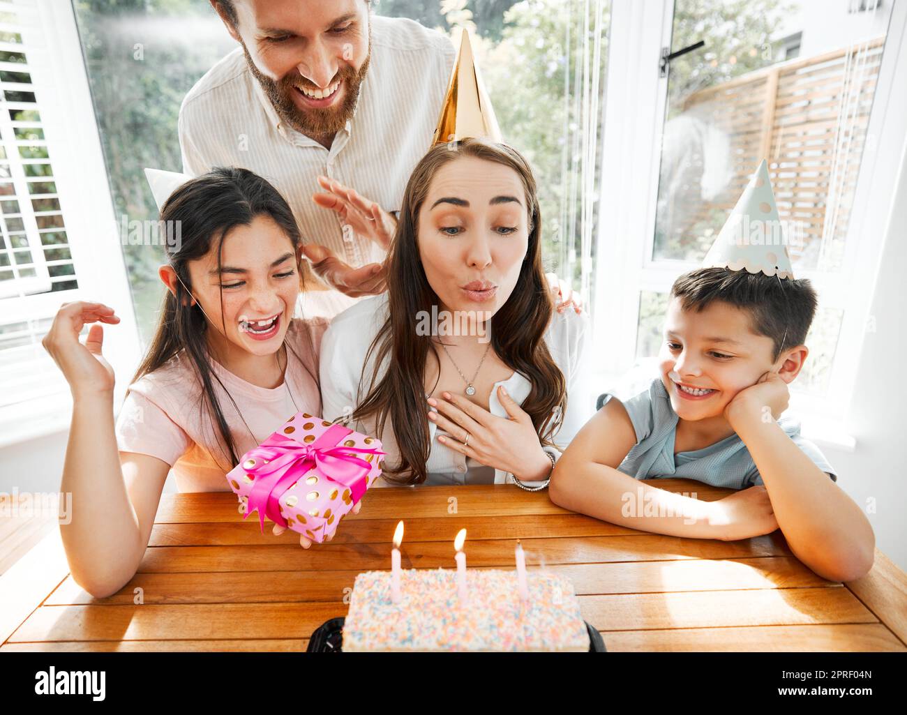 Geburtstag, Familie und Feier mit einer Frau, die die Kerzen auf ihren Kuchen bläst. Ehemann und Kinder verwöhnen mom und sorgen dafür, dass sie sich an ihrem besonderen Muttertag wohlfühlt, während sie zu Hause eine Party feiern Stockfoto