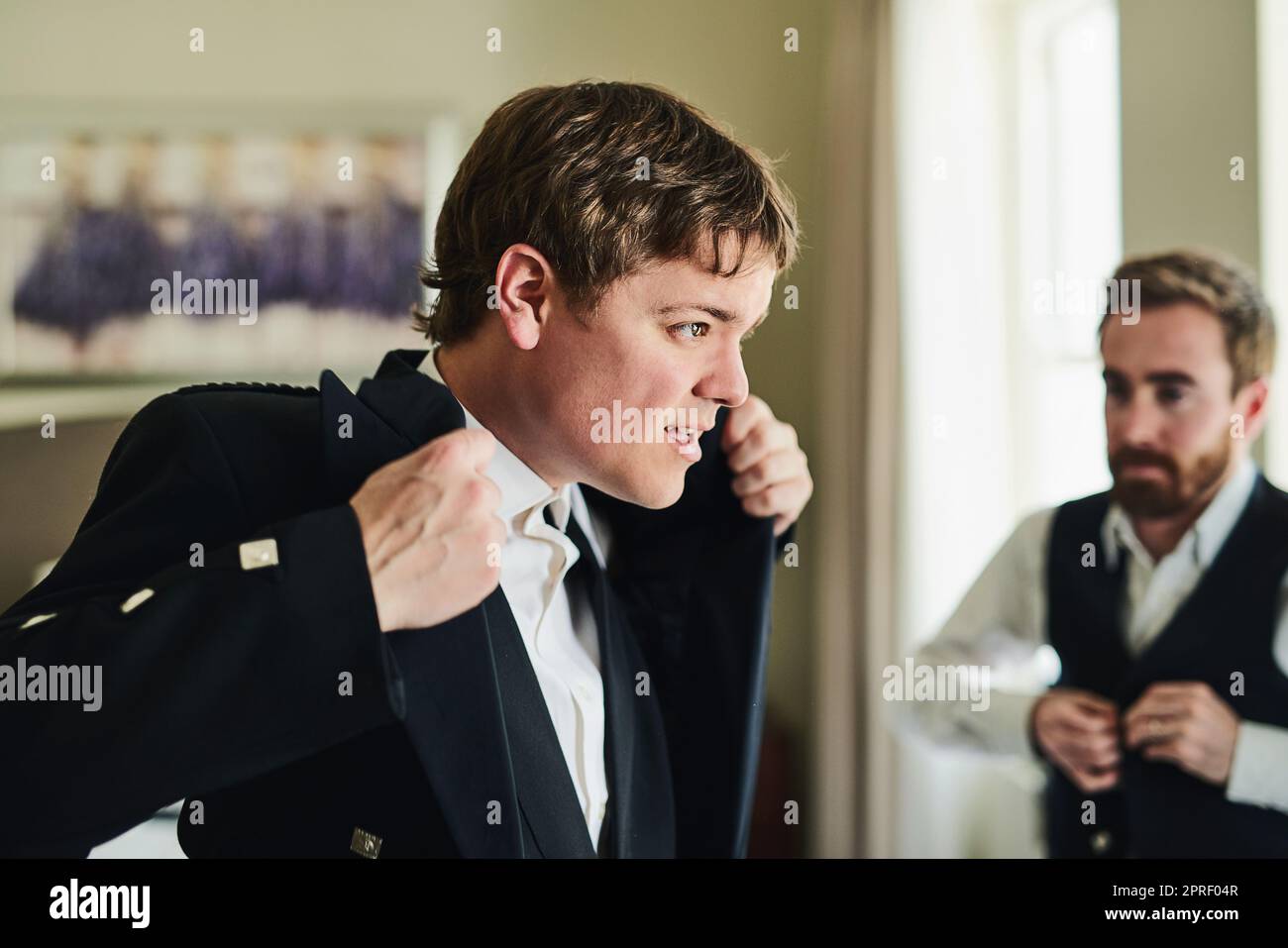 Vorbereitung auf seinen großen Tag. Ein selbstbewusster junger Mann, der eine Jacke anlegt, während er in einen Spiegel schaut, um sich für eine Hochzeit vorzubereiten. Stockfoto