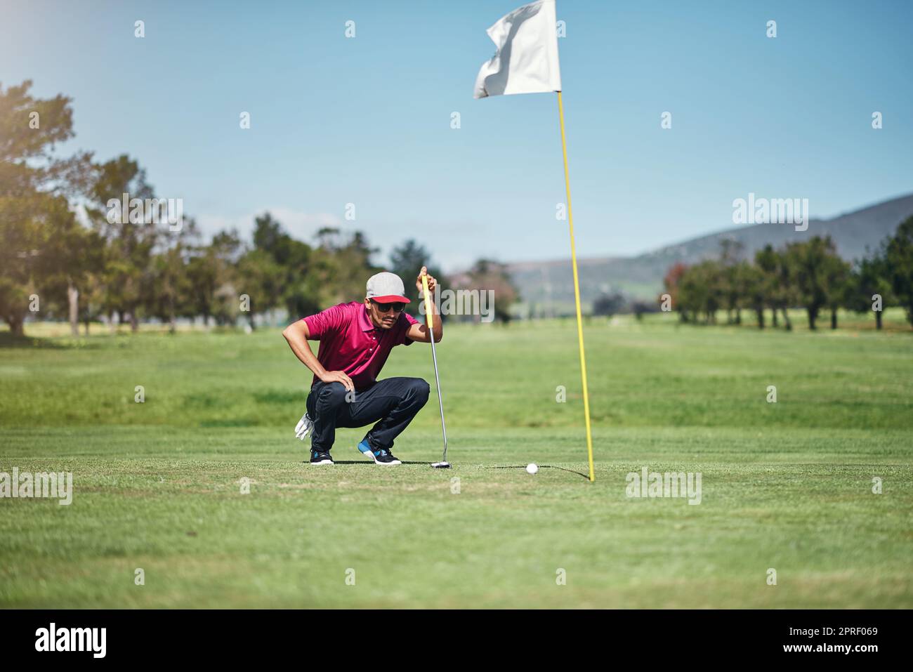 Ein fokussierter junger Golfer, der einen Golfball anschaut, während er tagsüber draußen auf dem Gras sitzt. Stockfoto