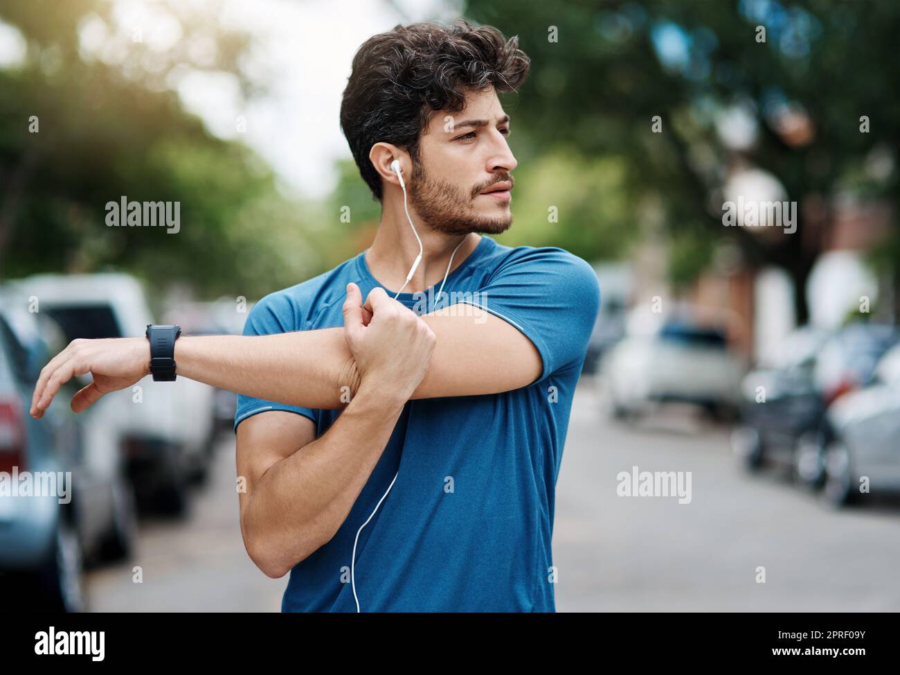 Es gibt ein paar Leute an diesem schönen Tag. Ein sportlicher junger Mann, der seine Arme während des Trainings im Freien streckt. Stockfoto