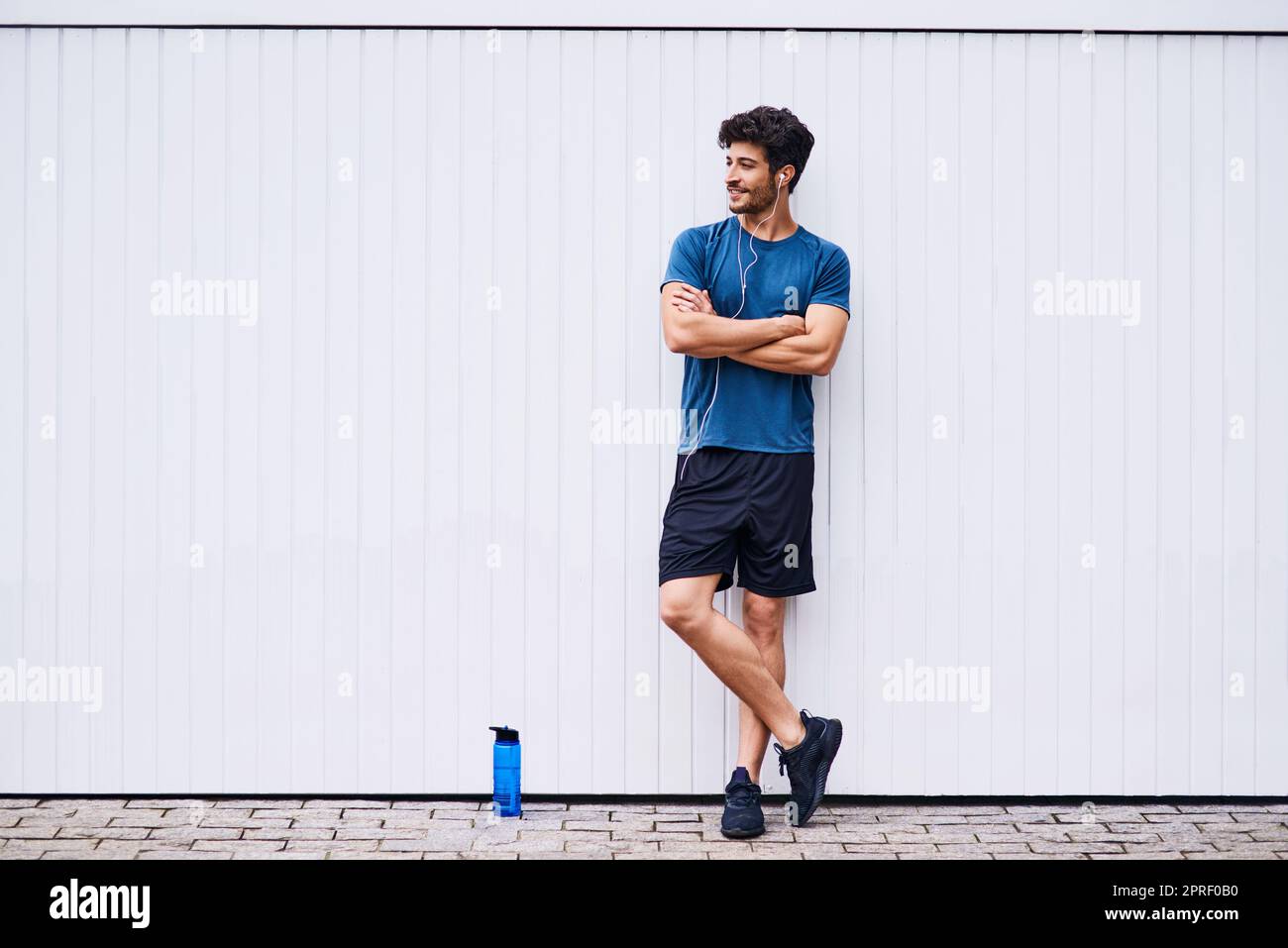 Ein cooles Gefühl von Casual während seiner Fitness-Reise. Ein sportlicher junger Mann, der an einer weißen Wand steht. Stockfoto