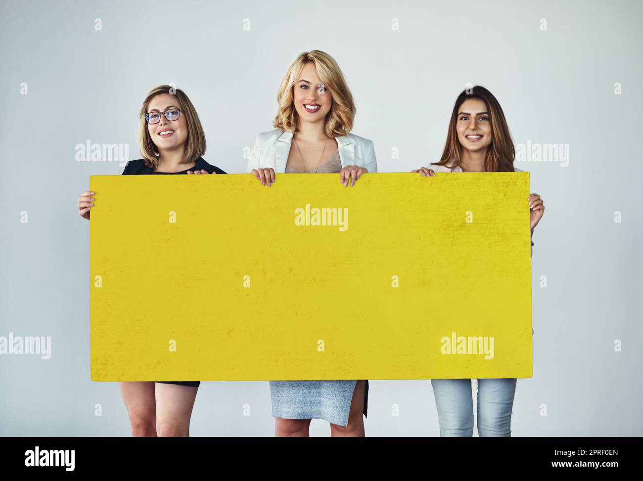 Das Vertrauen, Ihre Marke zu verkaufen. Studioaufnahme einer Gruppe von Geschäftsfrauen, die ein leeres gelbes Plakat hochhalten. Stockfoto