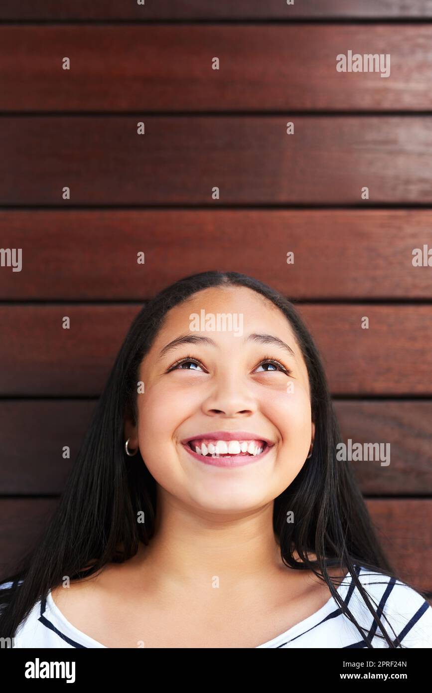 Seien Sie Ihre eigene Person, die Sie aufschauen. Ein glückliches junges Mädchen posiert vor einem hölzernen Hintergrund und schaut nach oben. Stockfoto