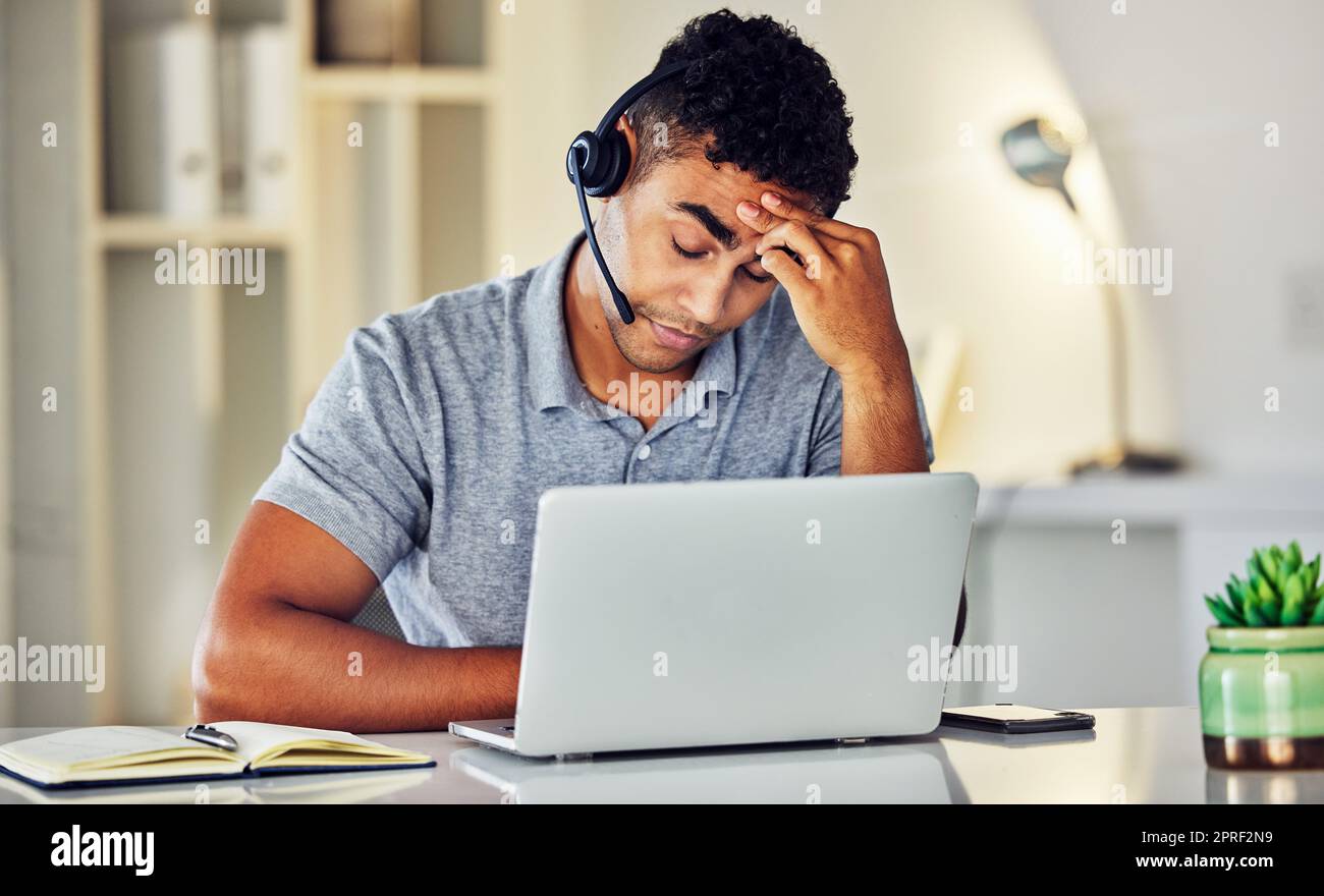 Gestresster, müder und frustrierter Callcenter-Agent fühlt sich im Büro krank oder krank, während er an seinem Laptop arbeitet. Ein besorgter und unglücklicher junger Telemarketing-Mitarbeiter, der unter Kopfschmerzen und Schmerzen leidet Stockfoto