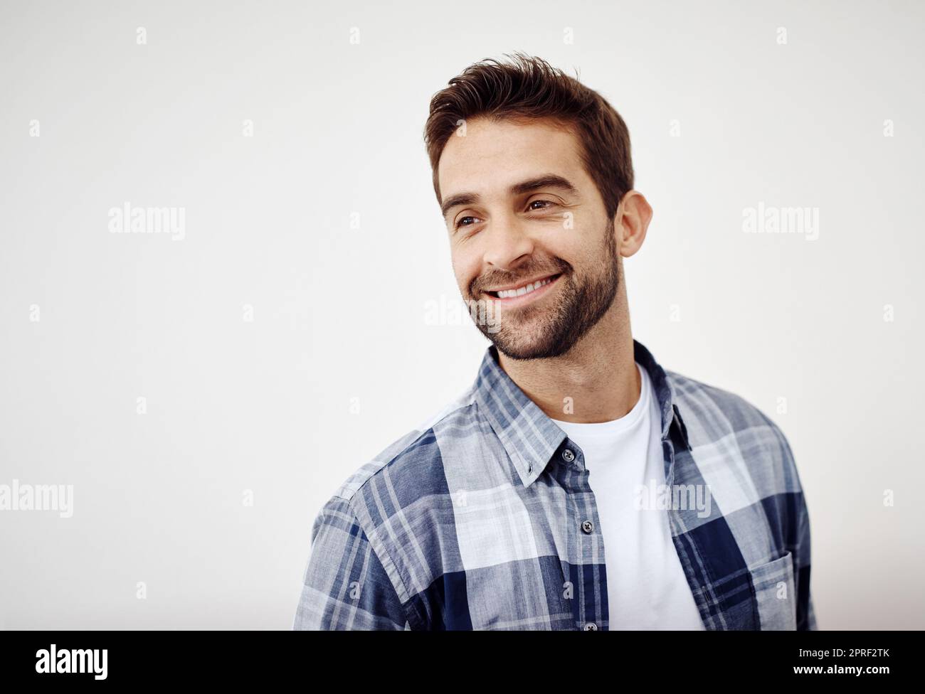 Lächelnd an eine Erinnerung. Studioaufnahme eines fröhlichen jungen Mannes, der vor einem weißen Hintergrund steht und direkt auf die Kamera blickt. Stockfoto