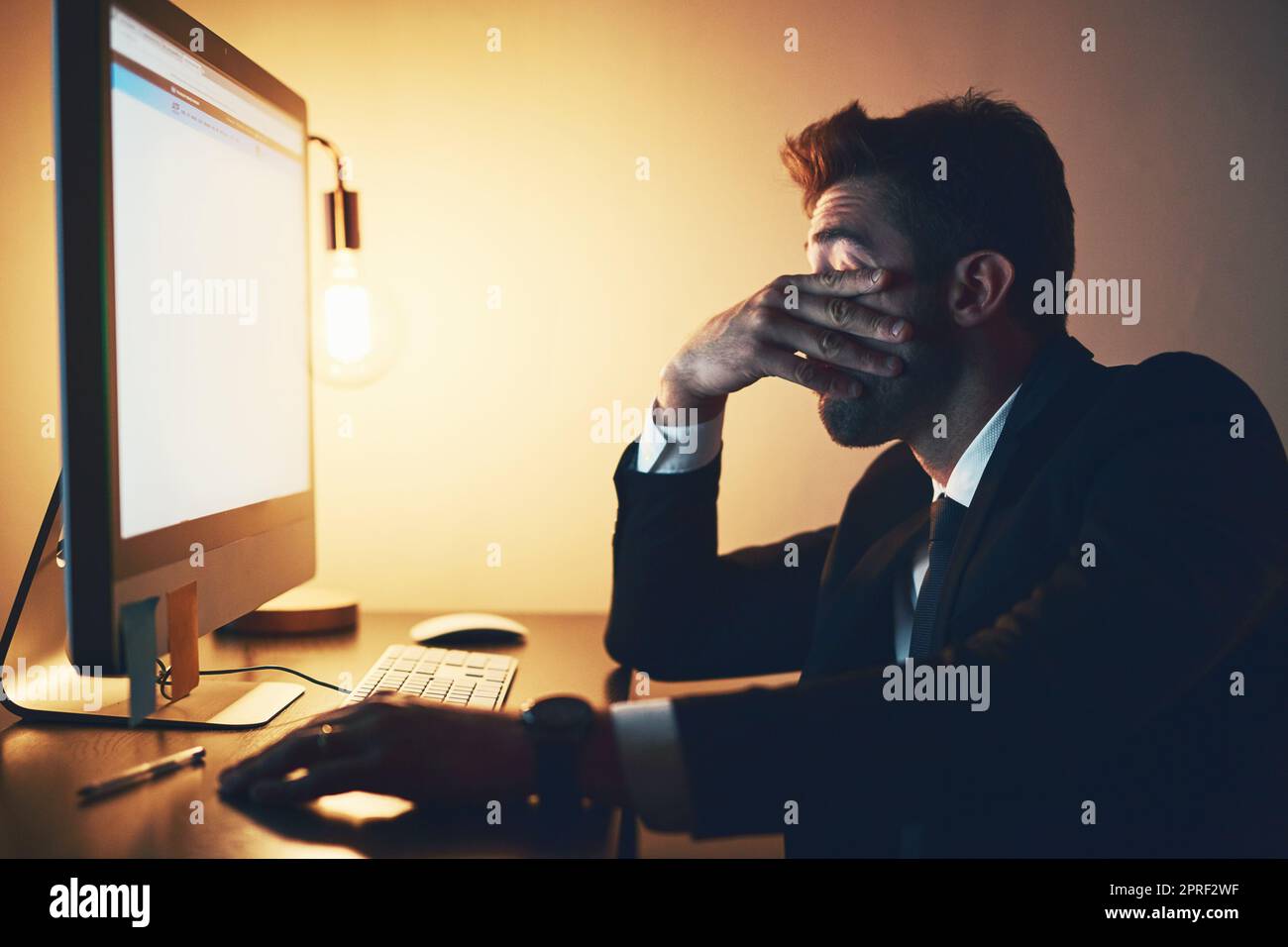 Fühlen Sie die Belastung. Ein junger Geschäftsmann, der gestresst aussieht, während er spät im Büro arbeitet. Stockfoto