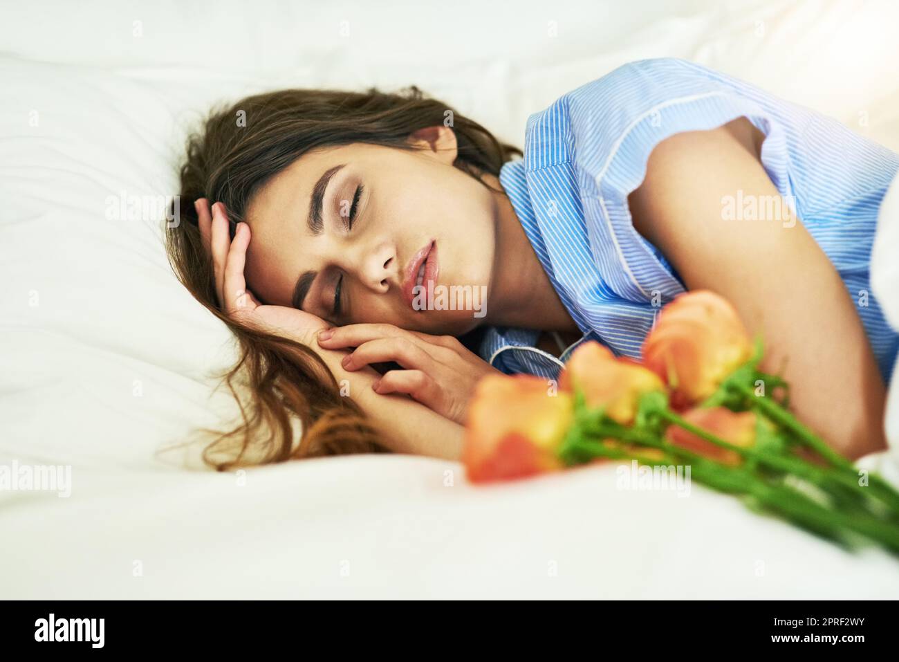 Shell erwachen zu einer netten Überraschung. Eine attraktive junge Frau schläft neben einigen Blumen in ihrem Bett. Stockfoto