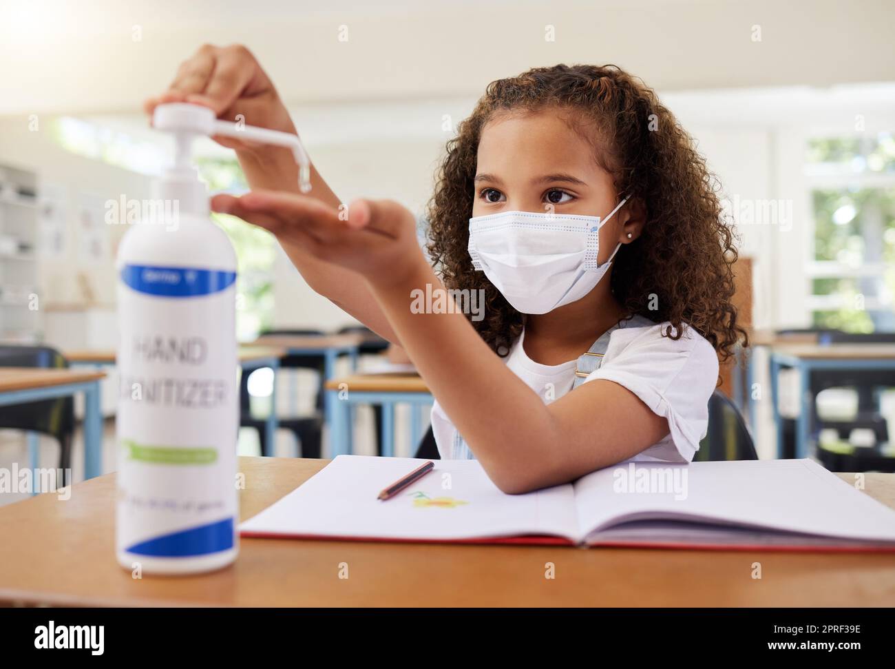 Desinfektionsmittel, heikle und saubere junge Frau in der Grundschule, die eine Maske in einem Klassenzimmer trägt. Ein Kind befolgt die Schutzbestimmungen von covid19, indem es seine Hände reinigt, um eine Infektion zu verhindern Stockfoto