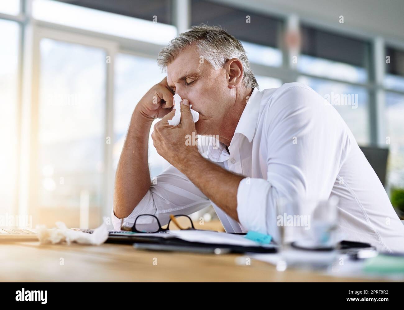 Ich könnte hier einschlafen. Ein reifer Geschäftsmann bläst seine Nase in das Büro. Stockfoto