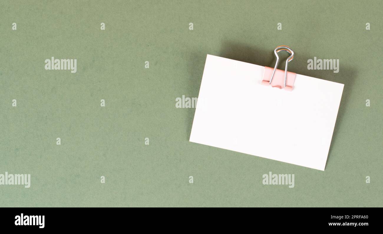 Leeres weißes Papier mit Büroklammer auf grünem Hintergrund, Platz für Text, Erinnerung oder Nachricht im Büro, Kommunikationskonzept Stockfoto