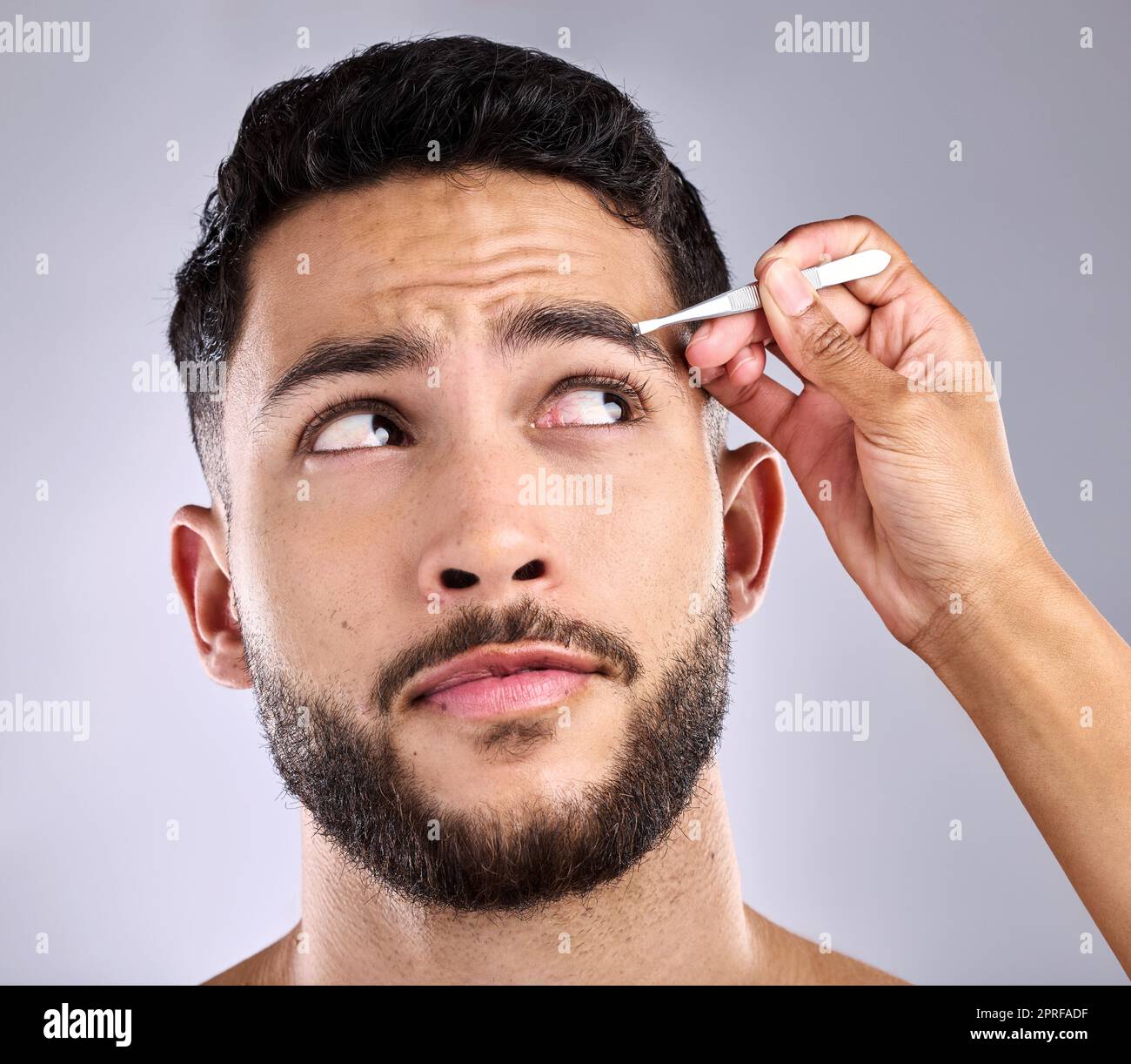 Ich würde es lieber hinter mich bringen. Nahaufnahme eines jungen Mannes, der vor grauem Hintergrund seine Augenbrauen pflückt Stockfoto