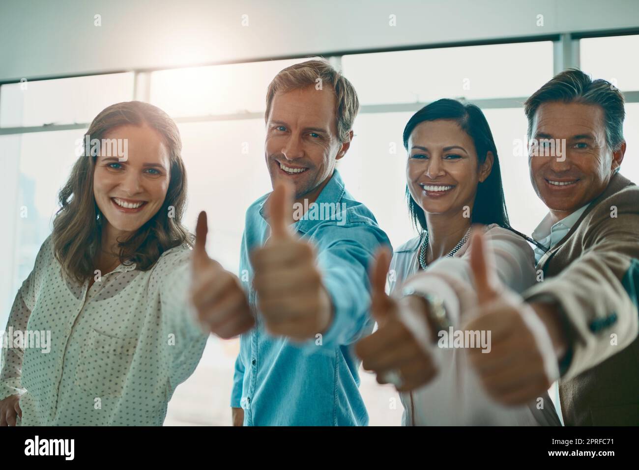 Motiviert und angefeuert. Eine motivierte Gruppe von Geschäftsleuten zeigt Daumen nach oben und lächelt, während sie die Kamera anschaut. Stockfoto