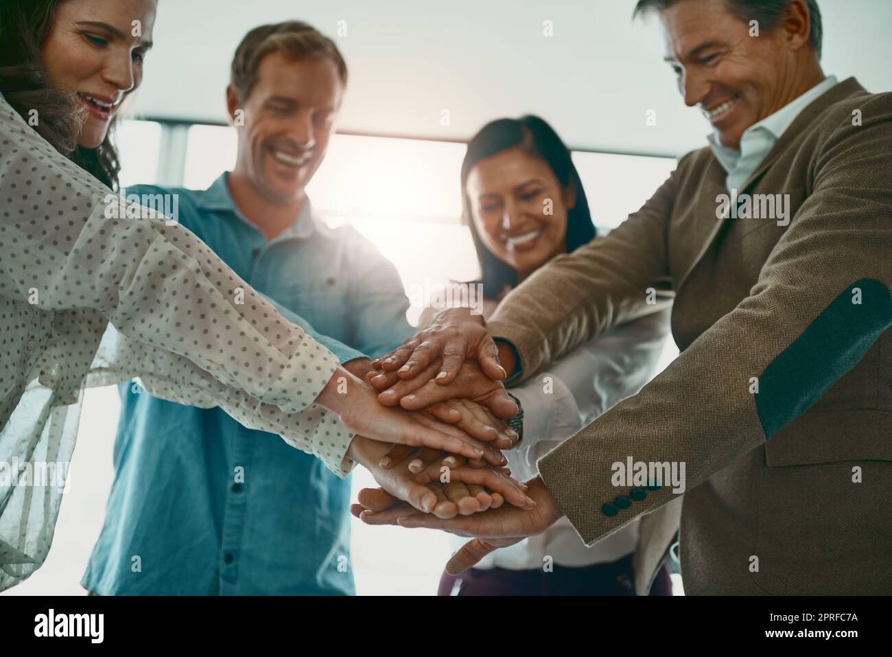 Hier geht es zum besten Team aller Zeiten. Eine motivierte Gruppe von Geschäftsleuten, die im Büro mit den Händen in einem Gespann stehen. Stockfoto