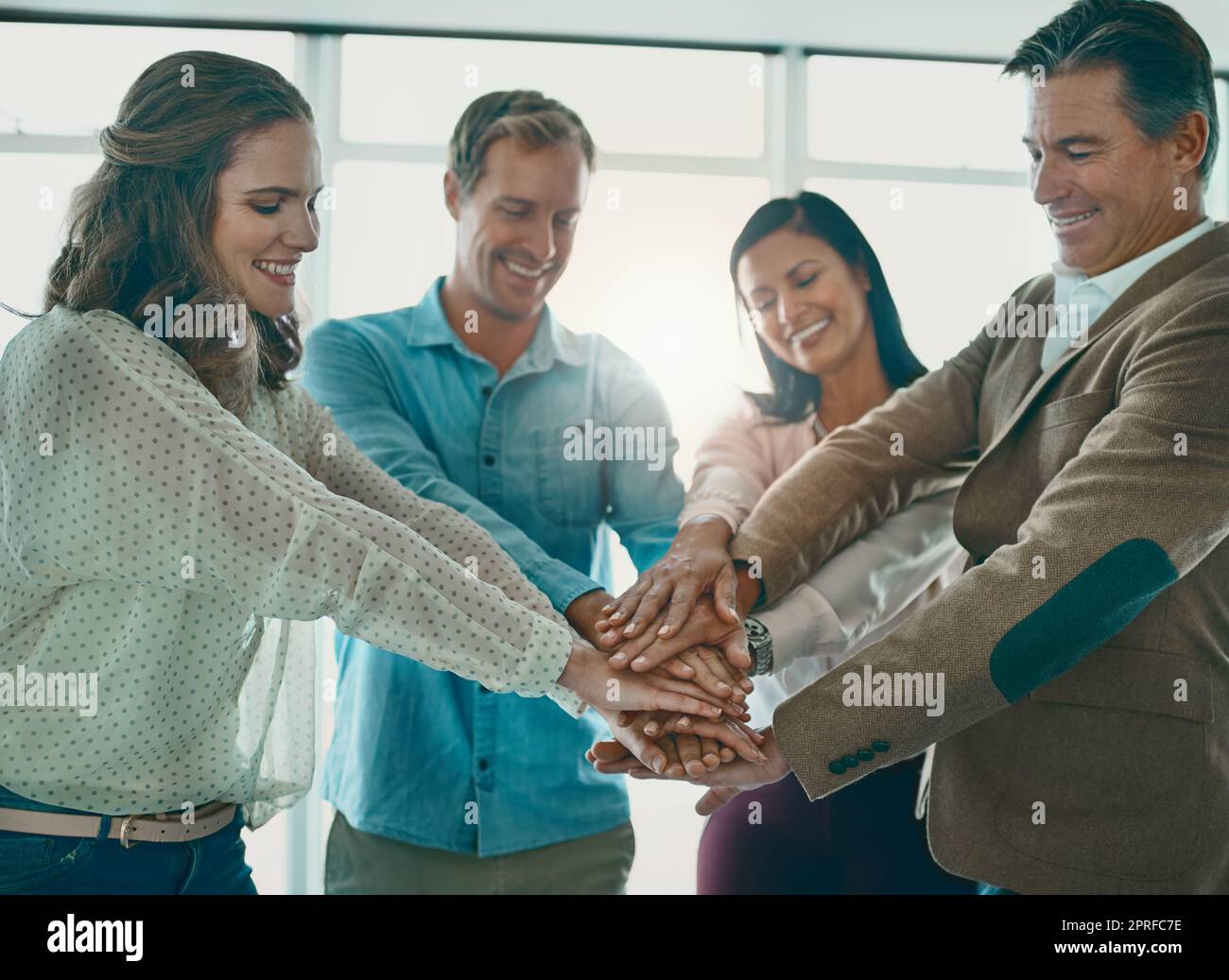Wir werden das zum Erfolg machen: Eine motivierte Gruppe von Geschäftsleuten, die mit den Händen im Büro stehen. Stockfoto