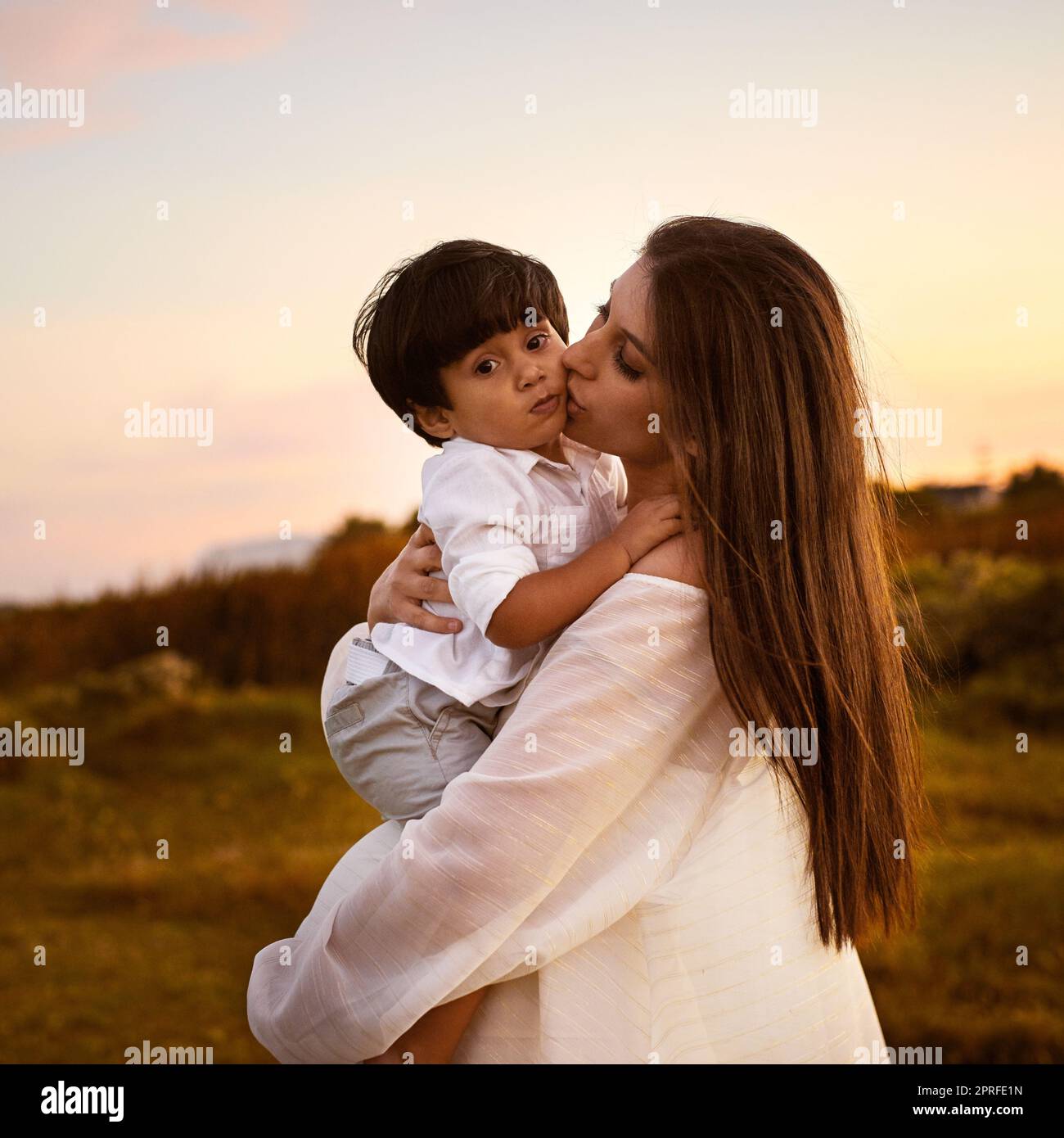 Mutter und Sohn, eine Bindung, die nie gebrochen werden kann. Eine junge Mutter küsst ihren Sohn auf der Wange im Freien. Stockfoto
