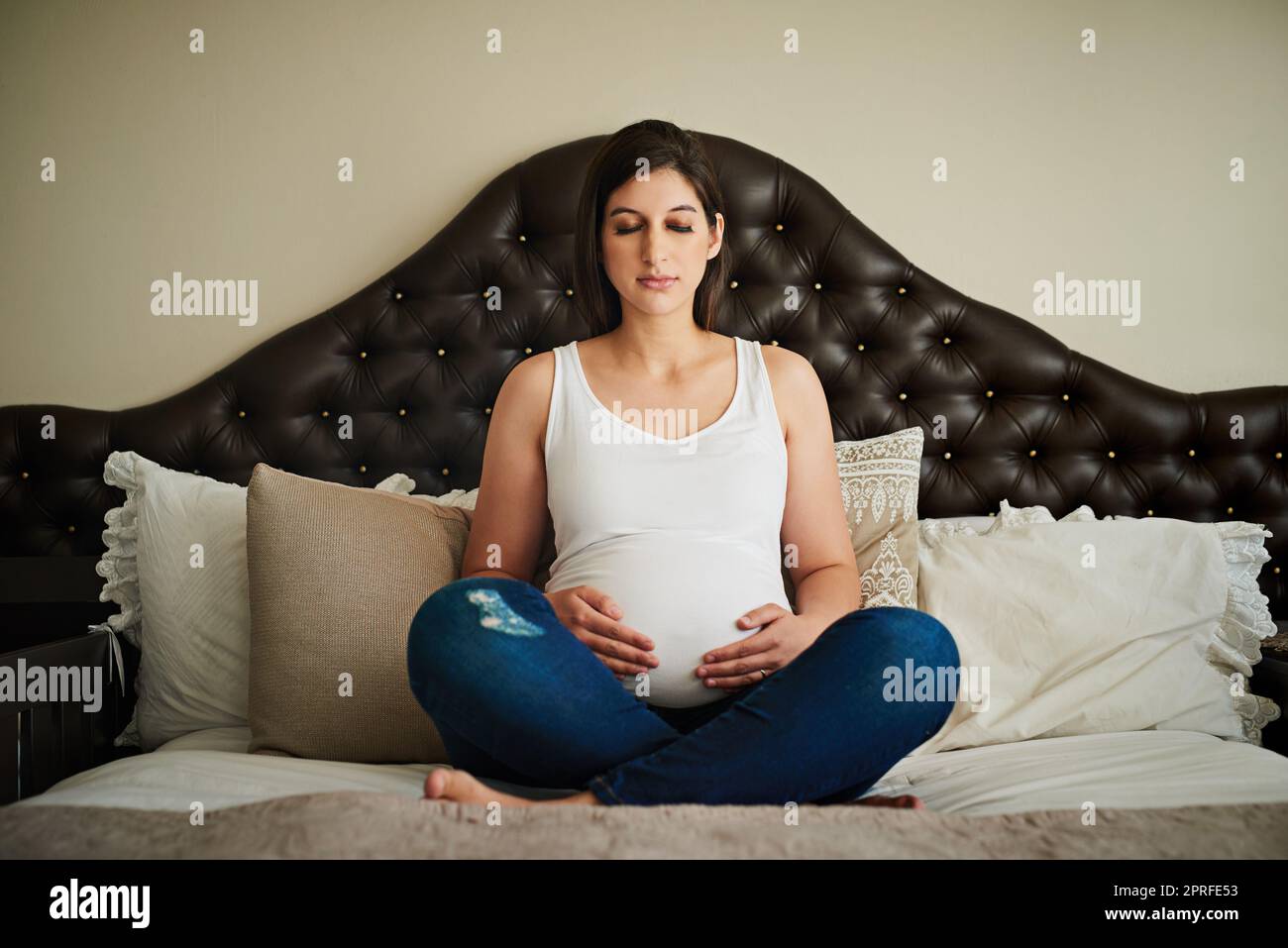 Eine Schwangere meditiert auf ihrem Bett, während sie ihren Bauch verkrammt. Stockfoto