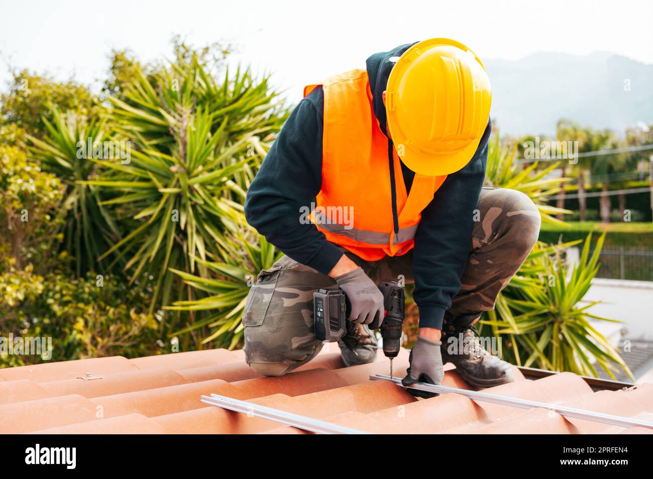 Der technische Arbeiter arbeitet mit dem Bohrer auf dem Dach eines Hauses Stockfoto