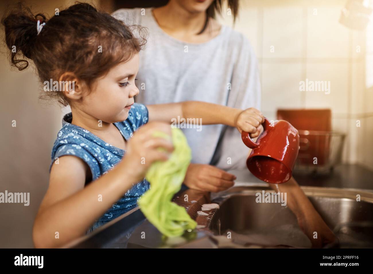 Ein glückliches kleines Mädchen und ihre Mutter waschen das Geschirr zu Hause. Stockfoto