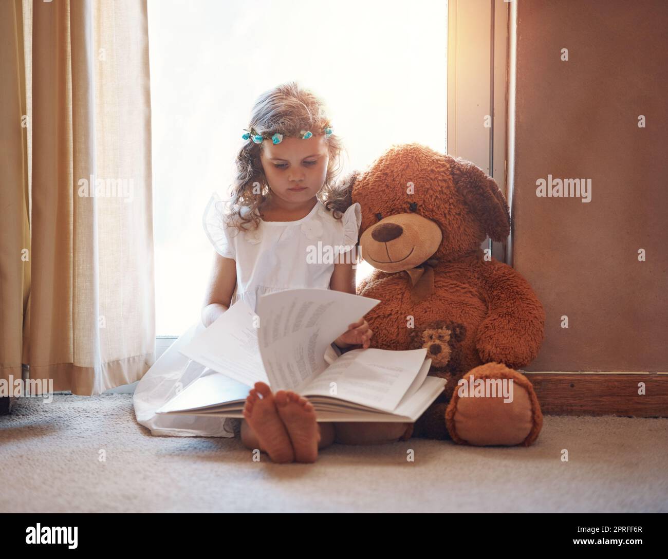 Worte wecken die Neugier und Phantasie eines Kindes. Ein entzückendes kleines Mädchen, das zu Hause ein Buch mit ihrem Teddybären liest. Stockfoto