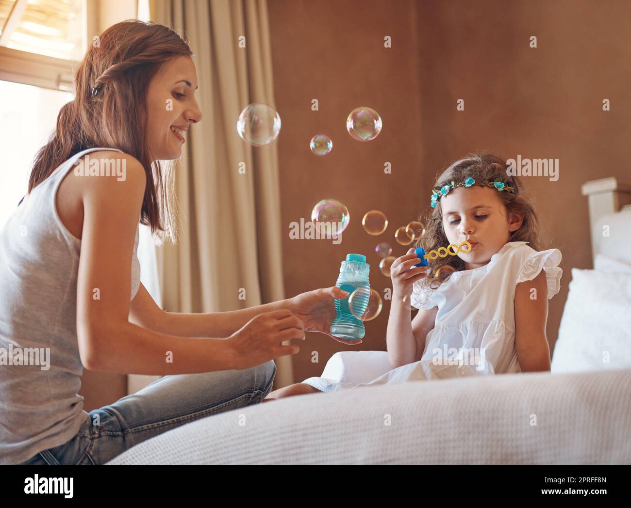 Eine Mutter und ihre kleine Tochter spielen zu Hause mit Blasen. Stockfoto