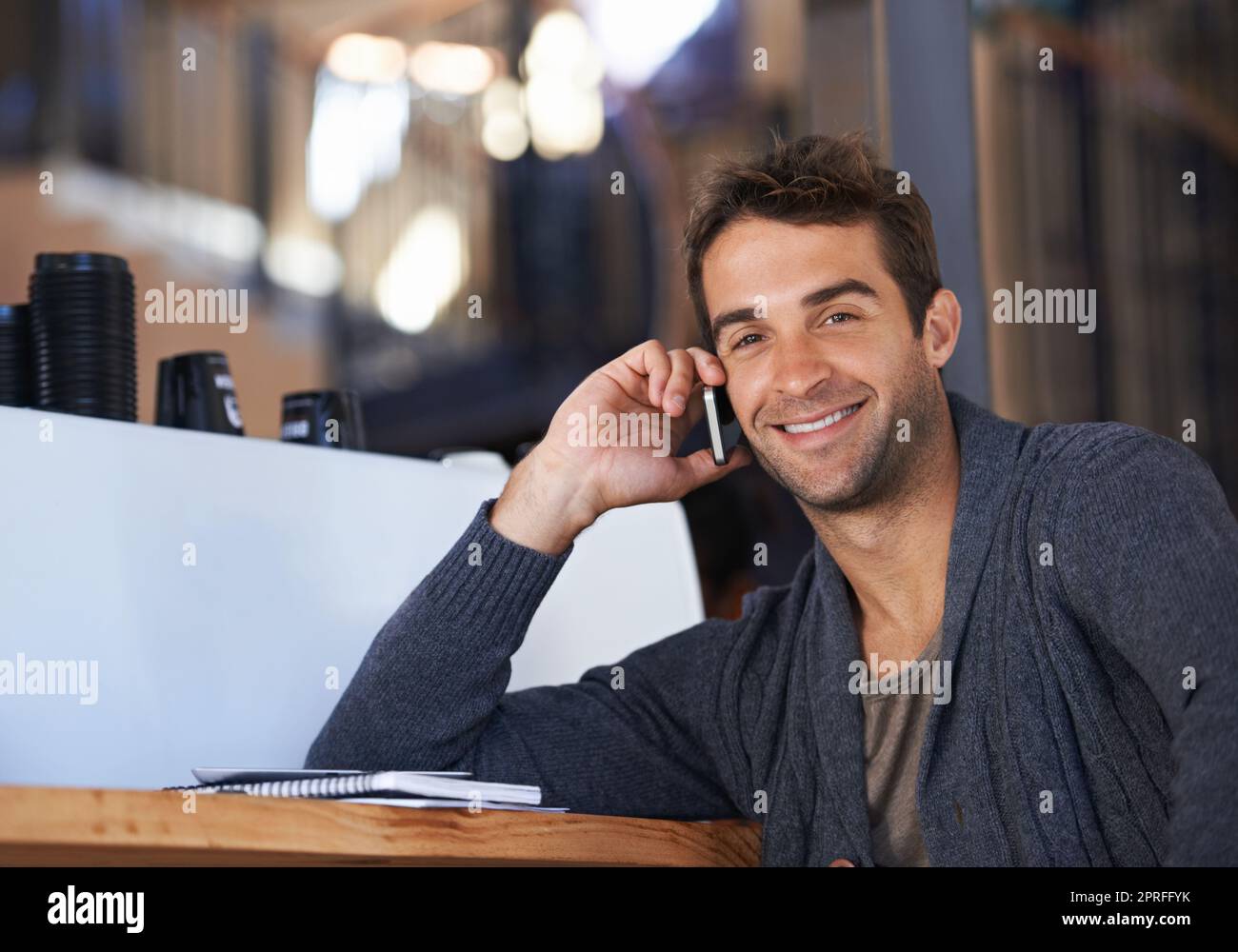 Ich rufe einen Freund auf einen Kaffee an. Ein junger Mann, der mit seinem Handy spricht, während er in einem Café sitzt Stockfoto