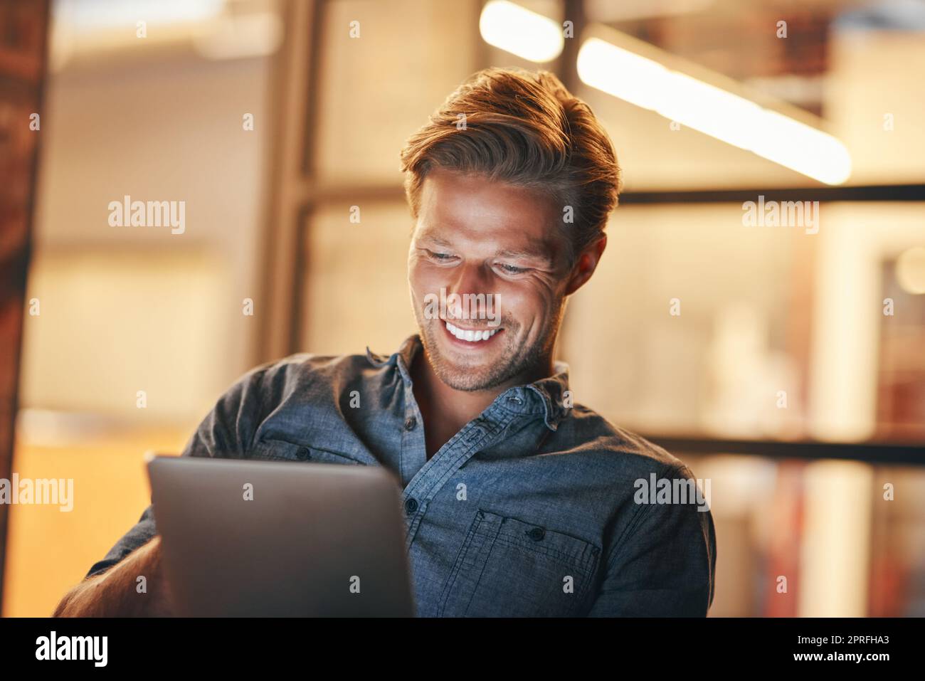 Digitalisieren Sie Aufgaben, um Zeit zu sparen. Ein hübscher junger Mann, der spät in seinem Büro arbeitet. Stockfoto