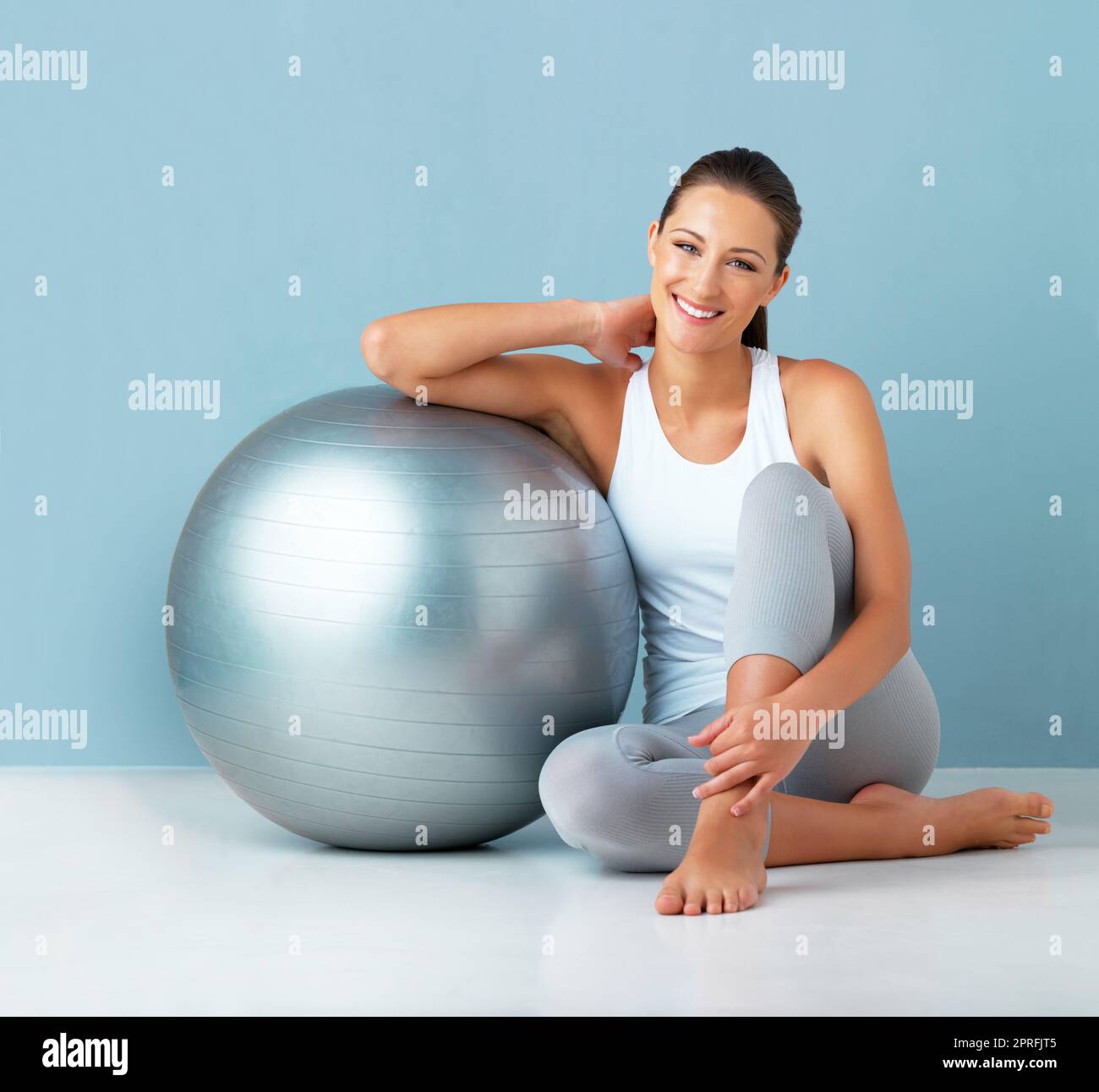 Es ist alles, was ich für ein Training brauche. Studioportrait einer gesunden jungen Frau, die sich vor blauem Hintergrund an einem Übungsball lehnt. Stockfoto