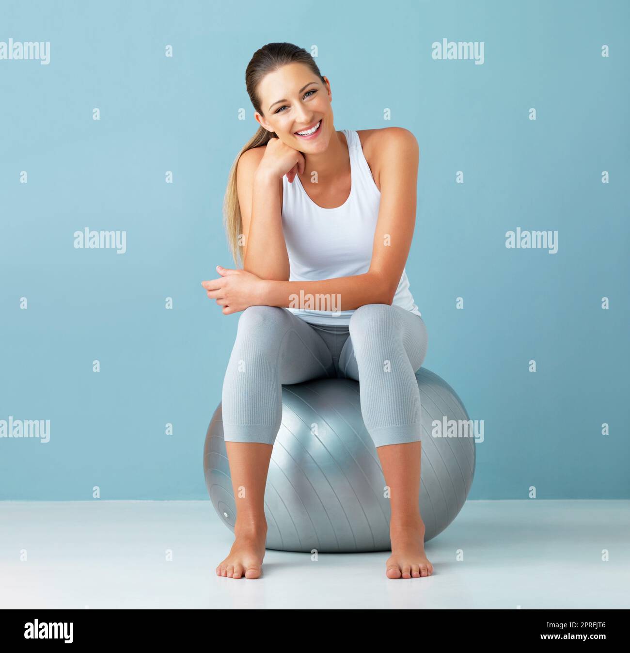 Dieser Ball begleitet mich zu jedem Workout. Studioportrait einer gesunden jungen Frau, die auf einem Übungsball vor blauem Hintergrund sitzt. Stockfoto
