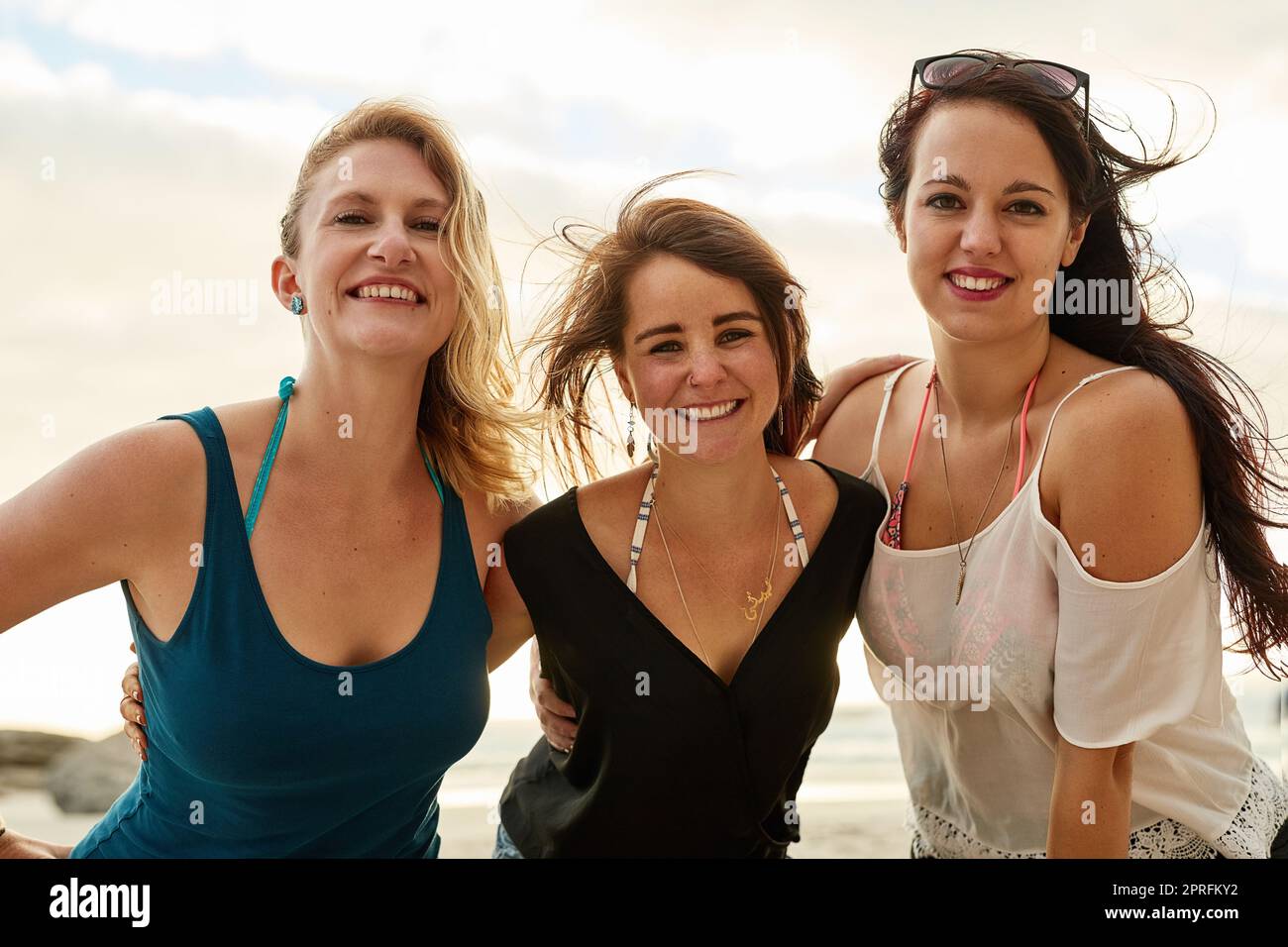 Sonnenschein und Lächeln am Meer. Porträt einer Gruppe glücklicher junger Freunde, die sich am Strand mit ihren Armen umeinander posieren. Stockfoto