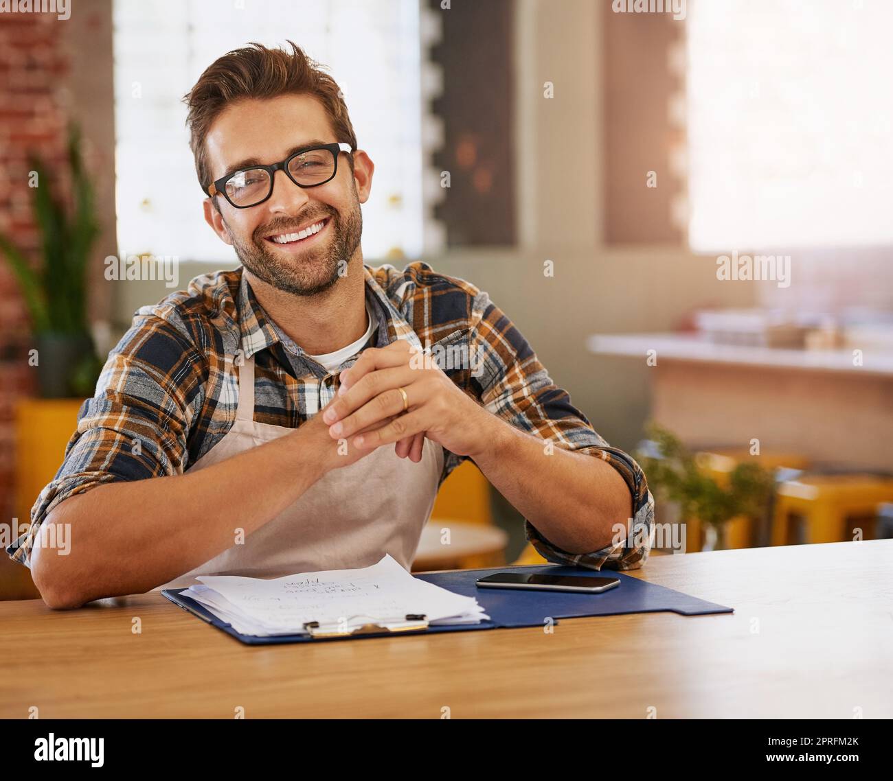 Einige Zeit im Coffee Shop zu verbringen. Porträt eines glücklichen jungen Geschäftseigentümers, der an einem Tisch in seinem Café Admin macht. Stockfoto