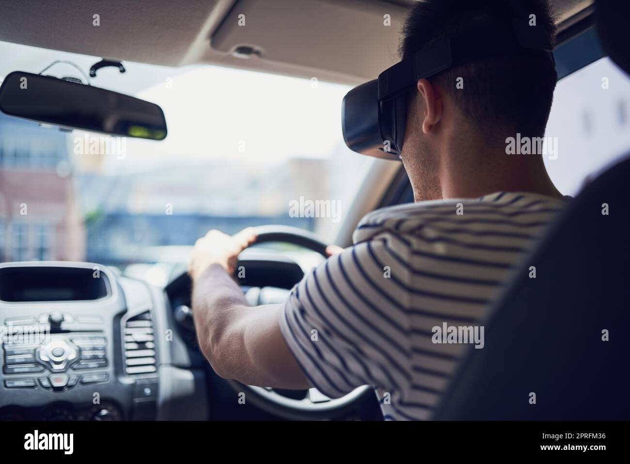 Sie werden sich im Straßenverkehr nie mehr langweilen. Ein glücklicher junger Mann, der ein Auto fährt, während er ein Virtual-Reality-Headset trägt. Stockfoto