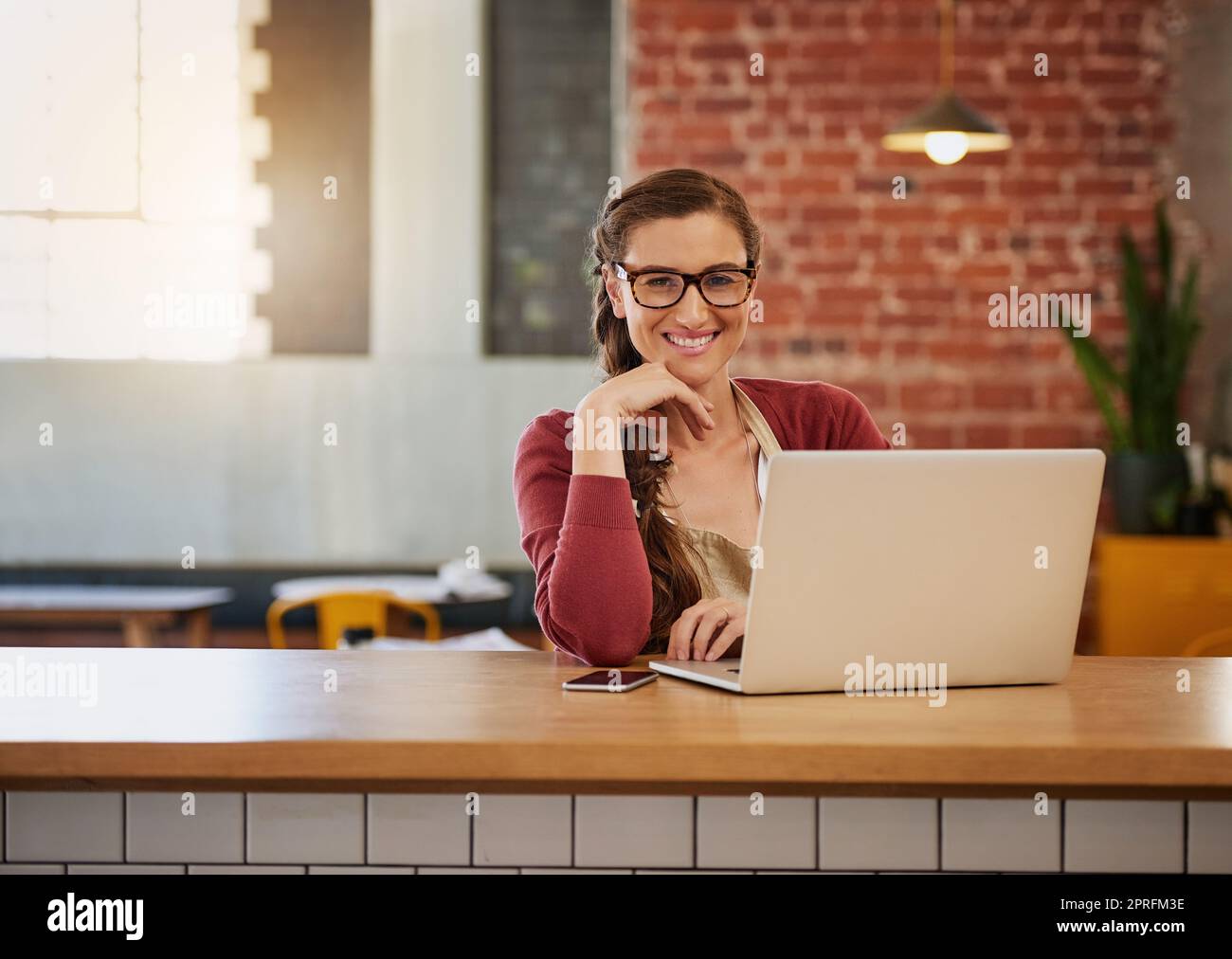 Ich verwandelte mein Café in einen WLAN-Hotspot. Porträt einer glücklichen jungen Geschäftsbesitzerin, die an einem Tisch in ihrem Café Admin macht. Stockfoto