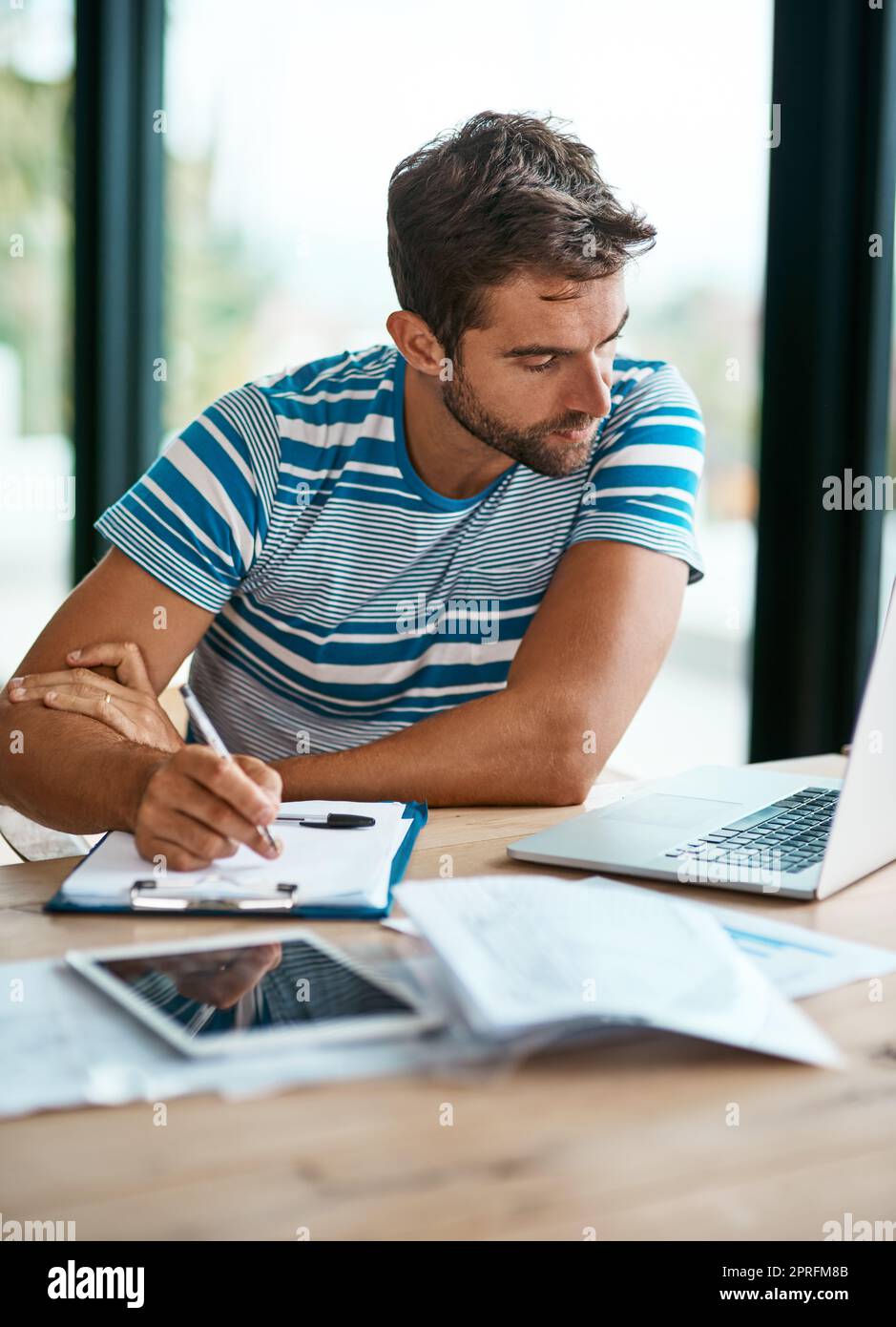 Tun einige schnelle Berechnungen. Ein hübscher junger männlicher Unternehmer, der Notizen macht, während er von seinem Heimbüro aus arbeitet. Stockfoto