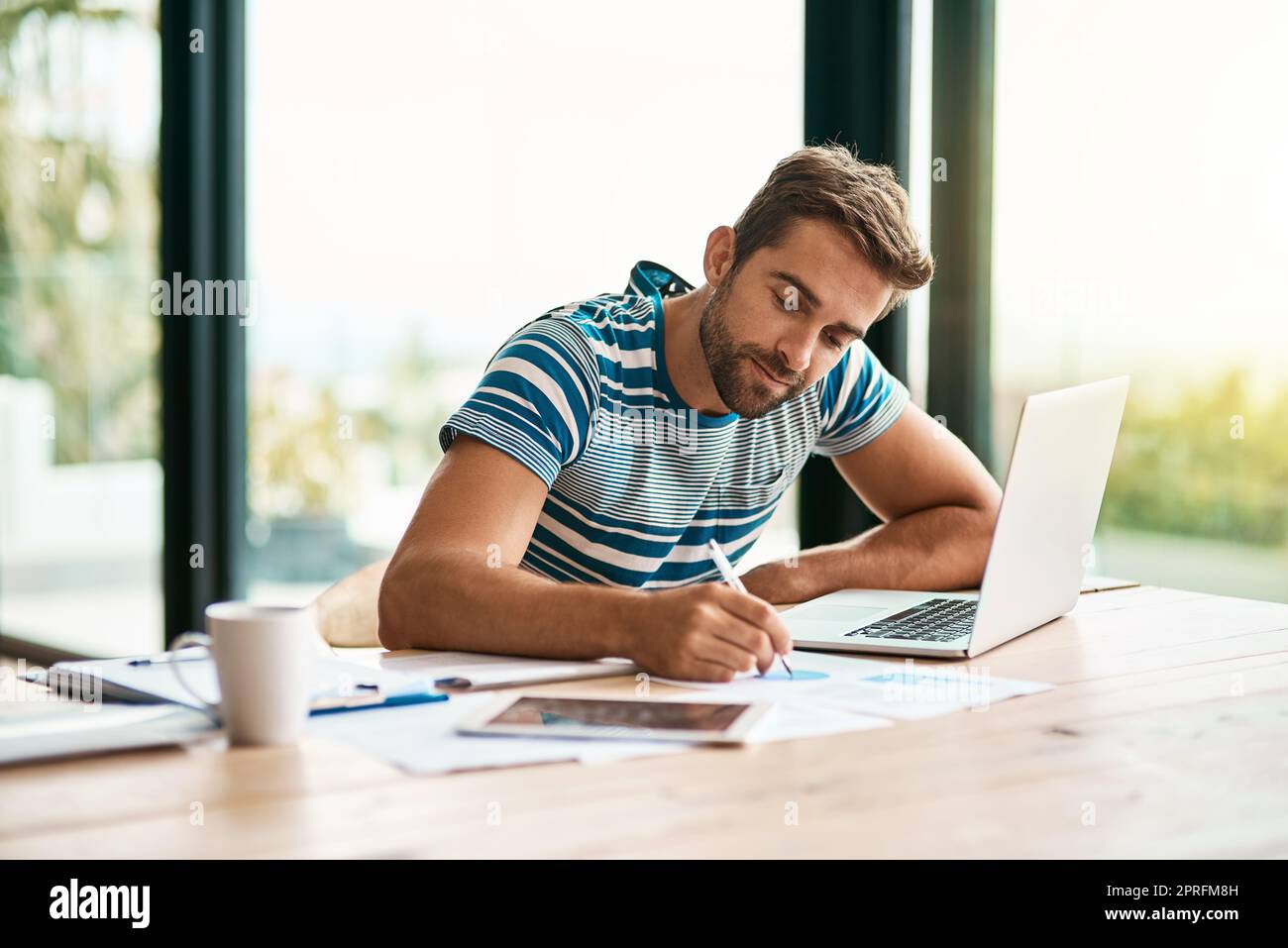 Er versucht, alles aufzuschreiben. Ein hübscher junger Unternehmer, der sich Notizen macht, während er von seinem Heimbüro aus arbeitet. Stockfoto