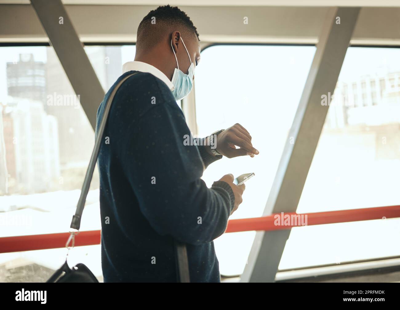 Ein Geschäftsreisender mit einer koviden Gesichtsmaske auf dem Weg zu einer Geschäfts- oder Geschäftschance in der Stadt. Junger schwarzer Geschäftsmann, der wegen der Verspätung am Flughafen 19 und der Einhaltung der Vorschriften verspätet ist Stockfoto