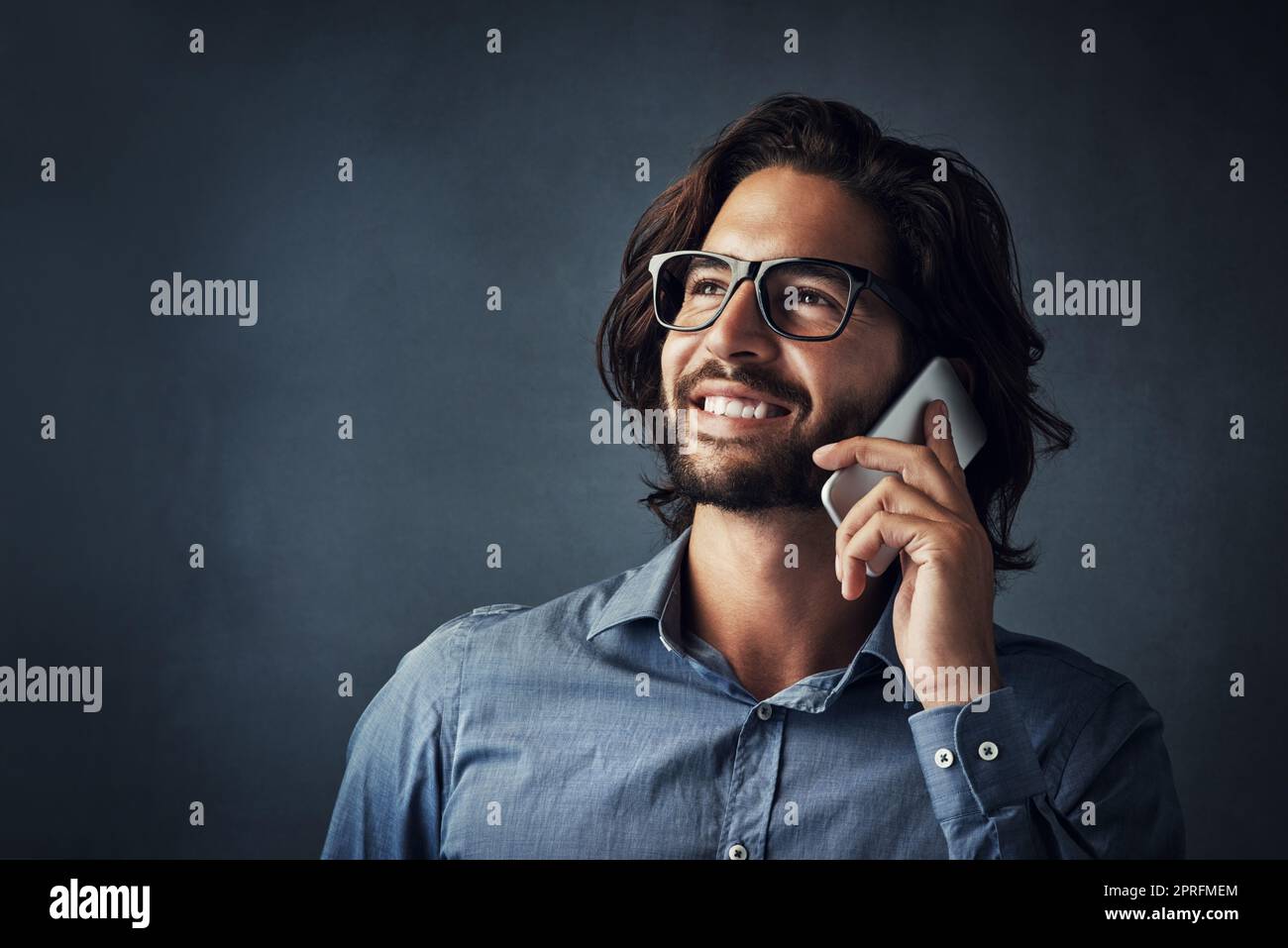 Ich rufe in Bezug auf deine Werbeanzeige an. Studio-Aufnahme eines hübschen jungen Mannes, der auf seinem Handy spricht, während er vor einem grauen Hintergrund steht. Stockfoto