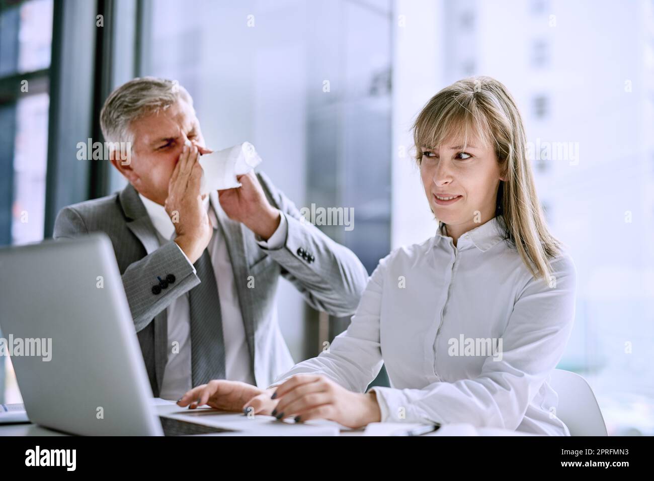 Entschuldigung, während ich niesen. Ein kranker Geschäftsmann niest vor einer Geschäftsfrau im Büro. Stockfoto