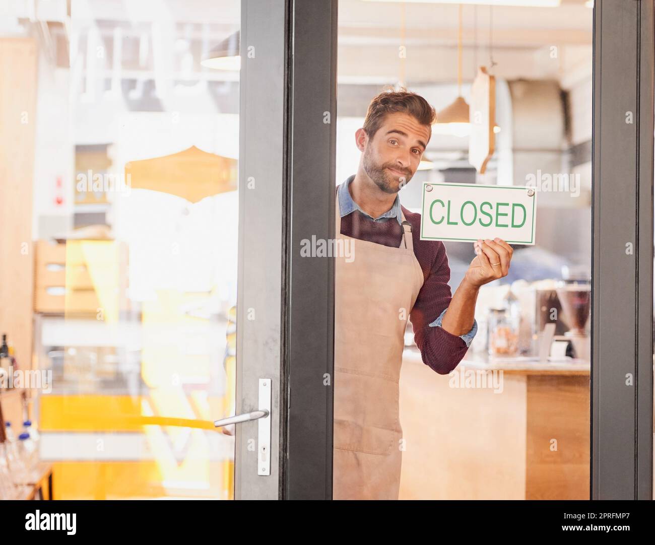 Sie schlummern, Sie verlieren. Porträt eines jungen Geschäftseigentümers, der ein geschlossenes Schild in das Fenster seines Cafés legt. Stockfoto