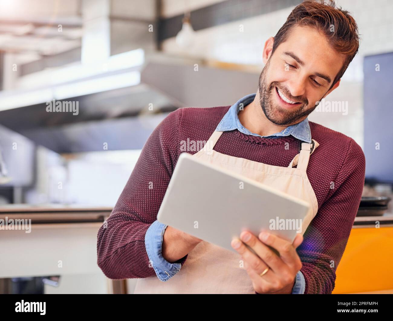 Zeit finden, um auf dem neuesten Stand zu bleiben. Glücklicher junger Unternehmer mit einem Tablet, während er in seinem Café steht. Stockfoto