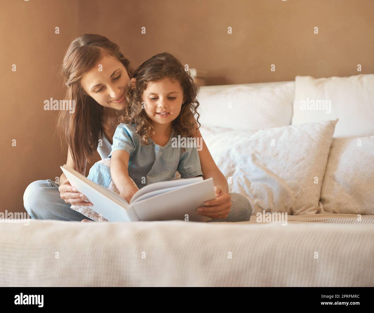 Eine glückliche Mutter und Tochter zu Hause beim Lesen eines Märchenbuches auf dem Bett. Stockfoto