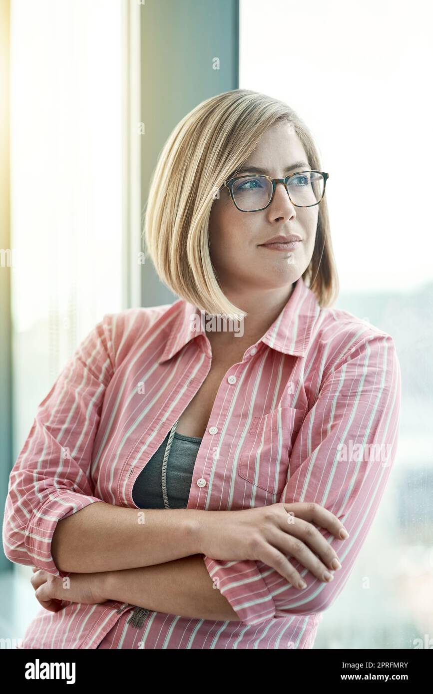 Verfolgen Sie weiter das außergewöhnliche: Eine Geschäftsfrau, die aus einem Büro aus dem Fenster schaut. Stockfoto