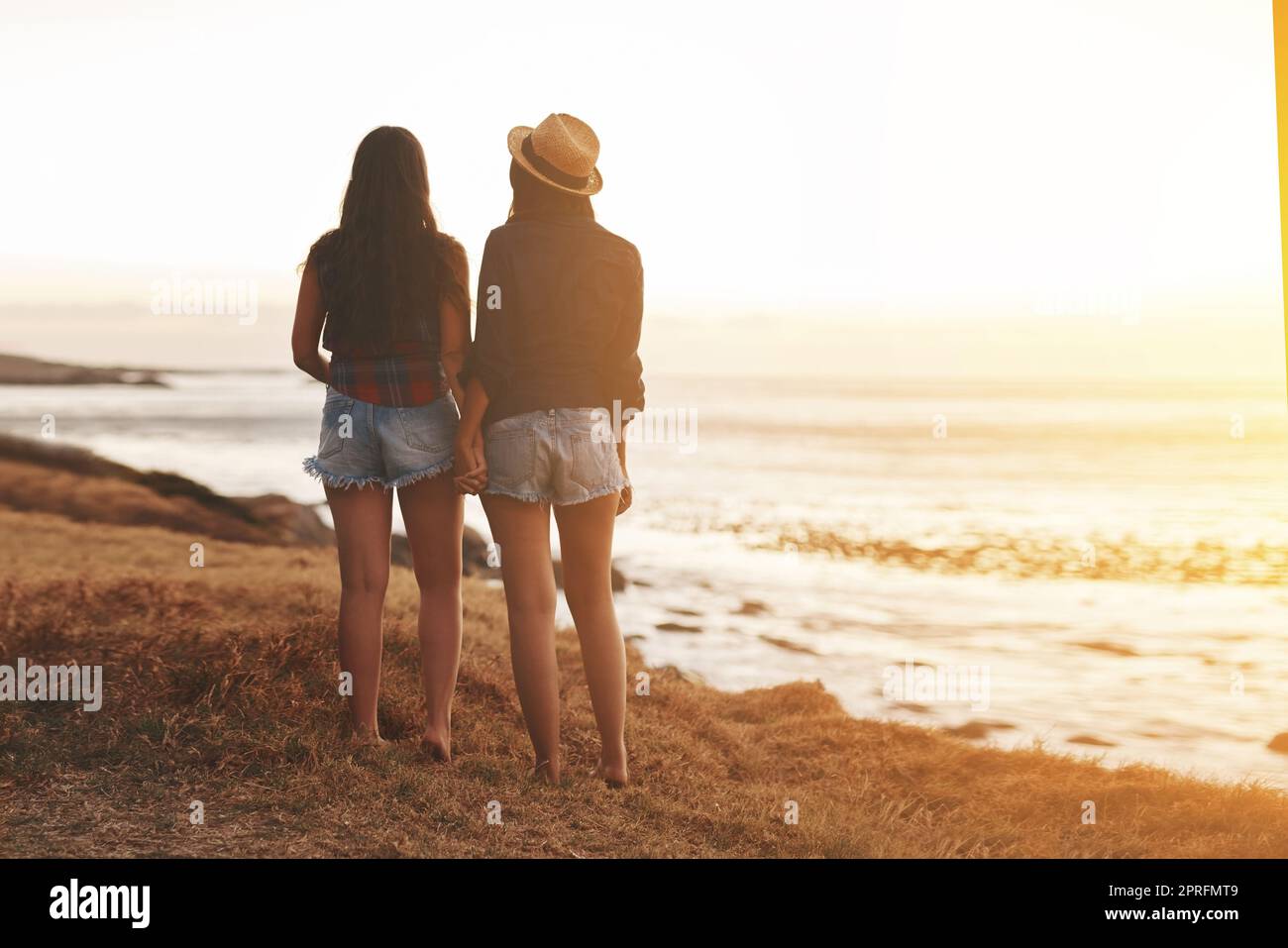 An der Küste war alles ruhig. Rückansicht von zwei jungen Freunden, die die Hände am Strand halten. Stockfoto