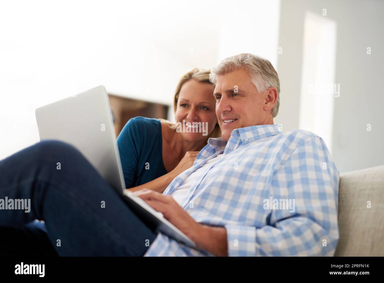 Surfen Sie online durch die weite Welt. Ein reifes Paar, das zu Hause einen Laptop benutzt. Stockfoto