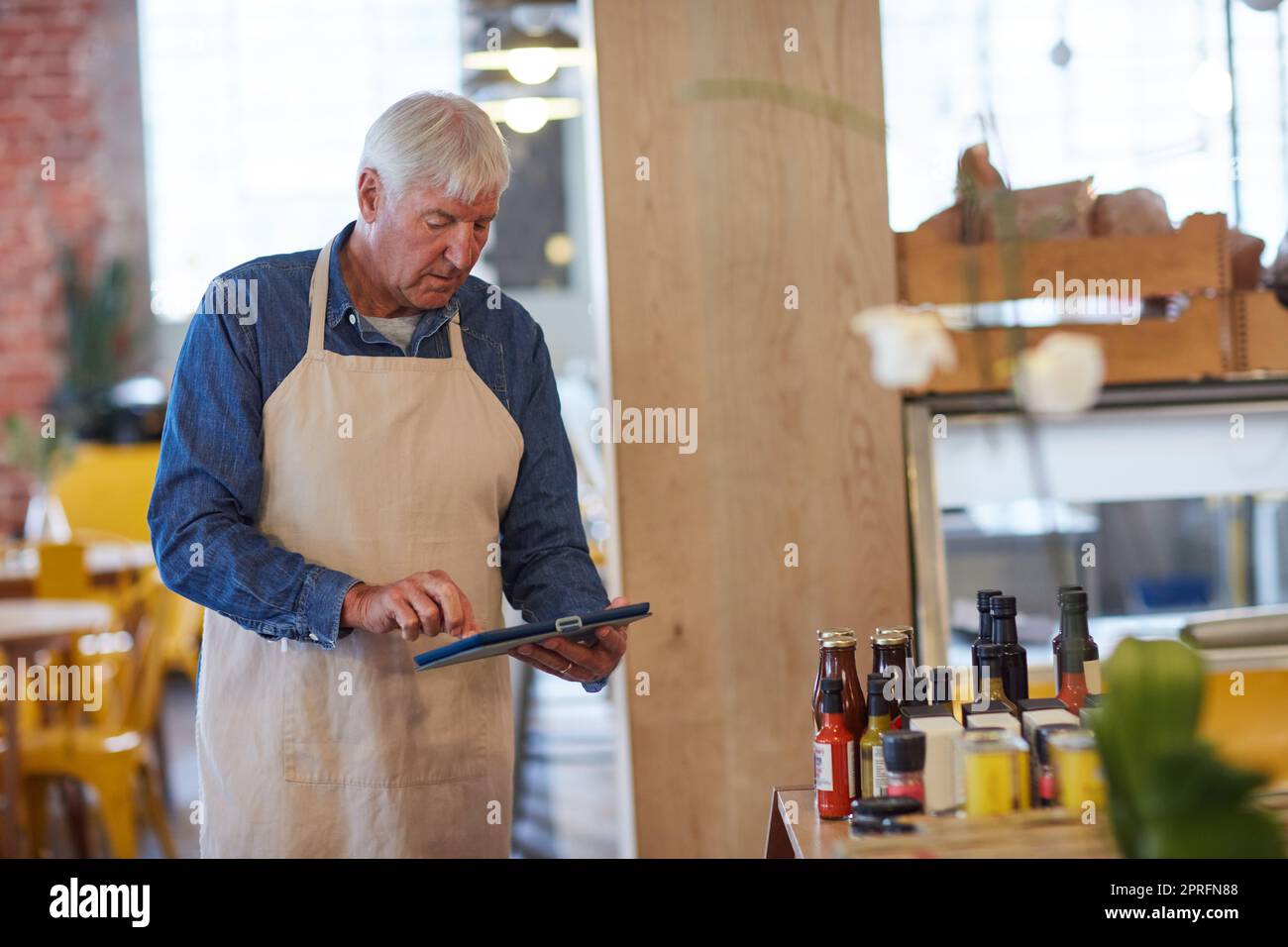 Aktienbehalter, vereinfacht. Ein glücklicher Senior-Unternehmer, der in seinem Café ein Tablet benutzt. Stockfoto