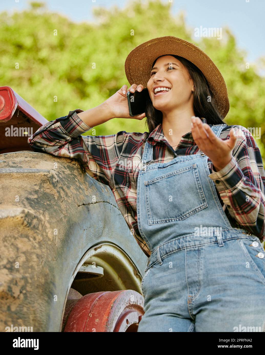 Landwirtschaft, Nachhaltigkeit und Landwirt, der telefoniert, während er auf einem Hof mit einem Traktor arbeitet. Wellness, Gesundheit und Agrofrau vernetzen sich mit einem mobilen Gerät, während sie auf dem Land stehen. Stockfoto