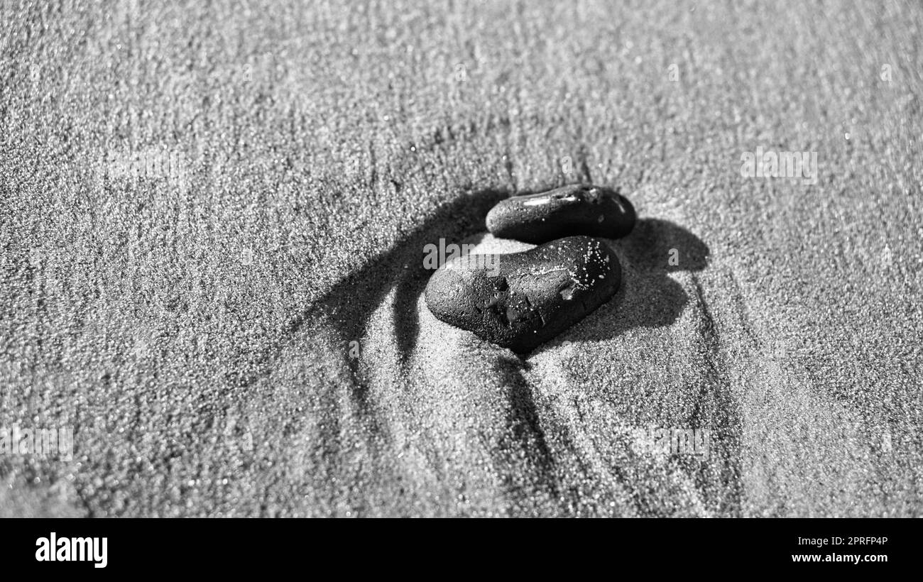 Herzförmiger Stein im Sand des Strandes an der Ostsee Schwarz-Weiß. Stockfoto