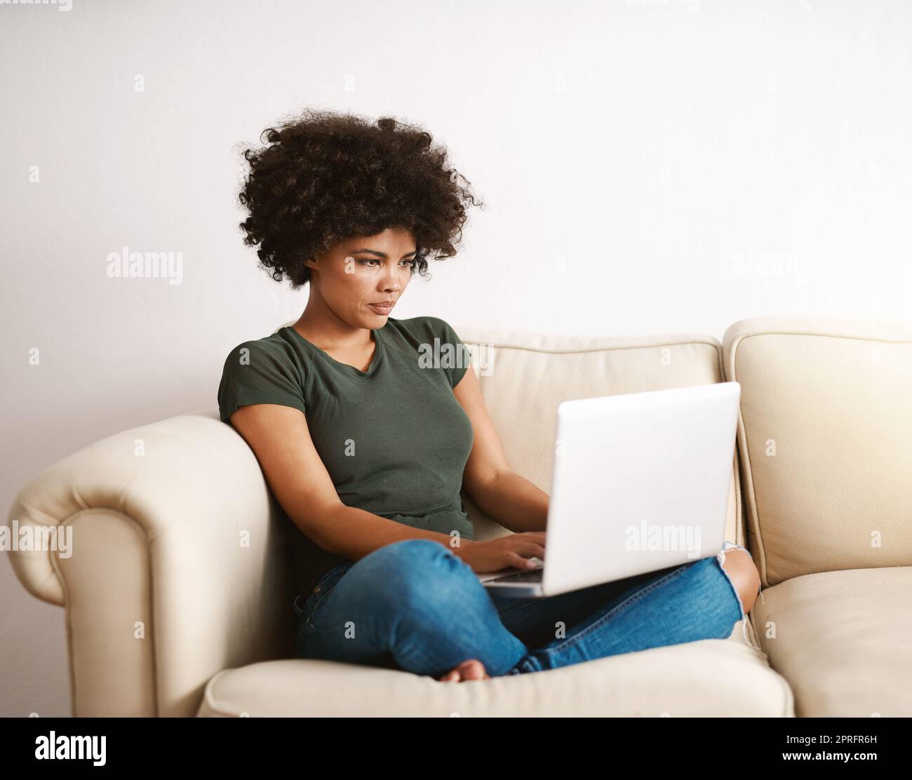 Die ein Büro braucht. Eine Frau, die ihren Laptop zu Hause mit gekreuzten Beinen auf dem Sofa benutzt. Stockfoto