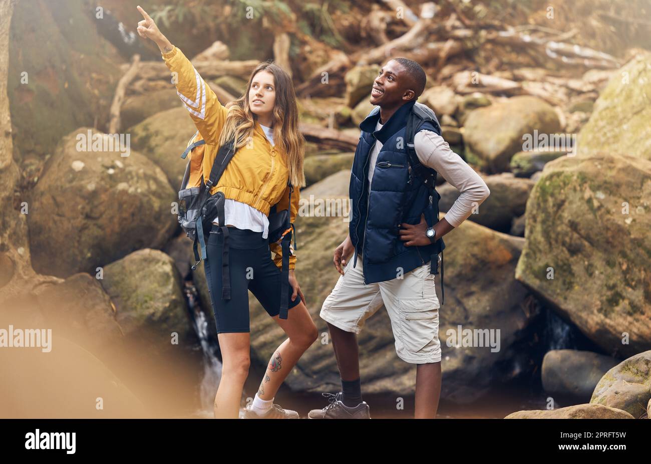 Fitness-Wandern, Natur und Paare beim Training, die gemeinsam nach Wegen suchen, um einen felsigen Pfad in der Natur zu nehmen. Mann und Frau aus verschiedenen Rassen zeigen auf Motivation und Navigation während der Wanderung. Stockfoto