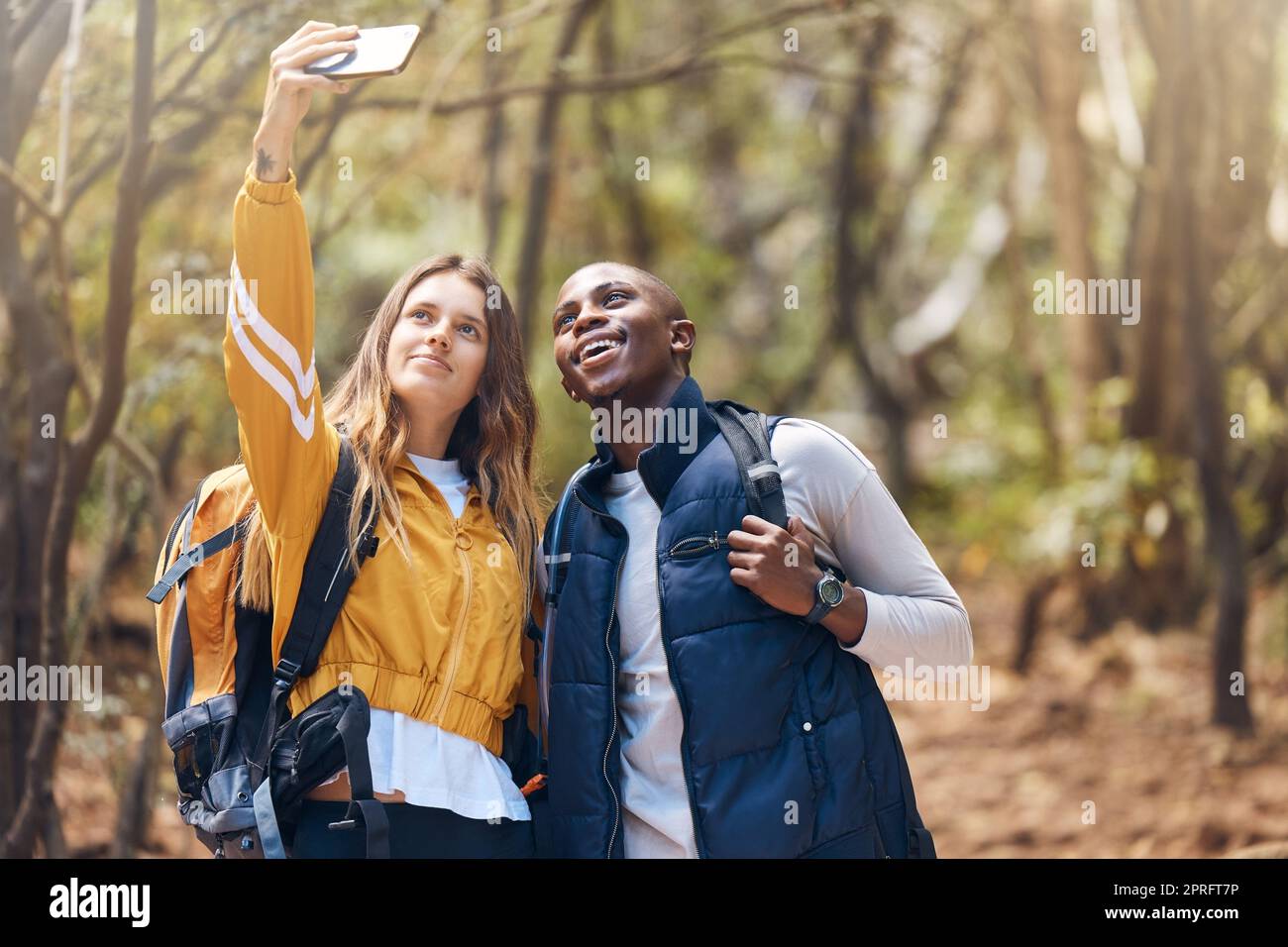 Selfie, glückliches Paar und Wanderabenteuer, während Sie Ihr Telefon für Urlaubsreisen in einem Wald oder Wald halten. Glücklich, Liebe und Bewegung in einer gesunden Beziehung zu schwarzem Mann und weißer Frau Stockfoto