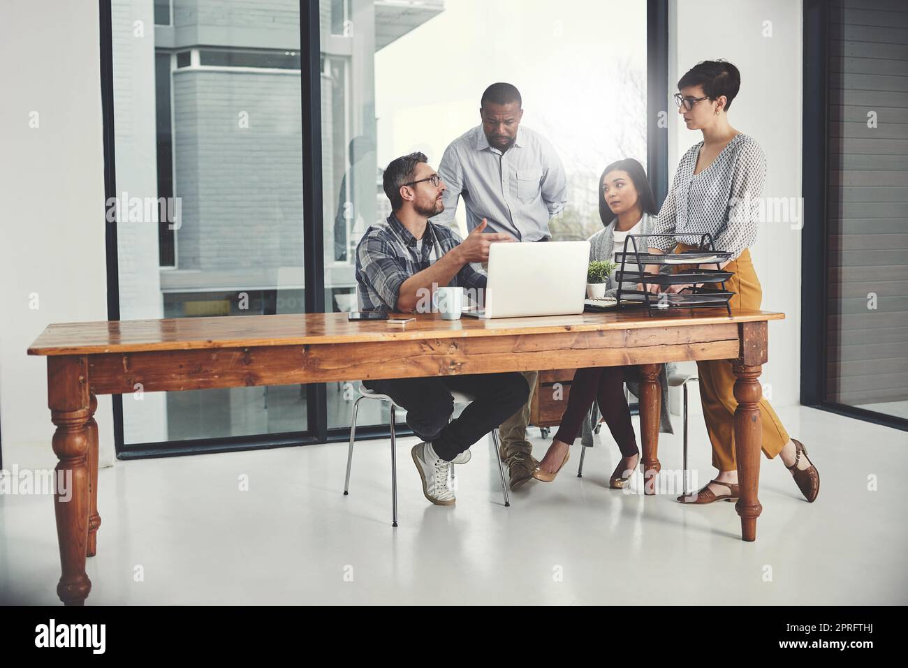 Zusammenarbeit auf dem Weg zum Erfolg. In voller Länge eine Gruppe von Geschäftsleuten, die sich in ihrem Büro um einen Laptop versammelten. Stockfoto